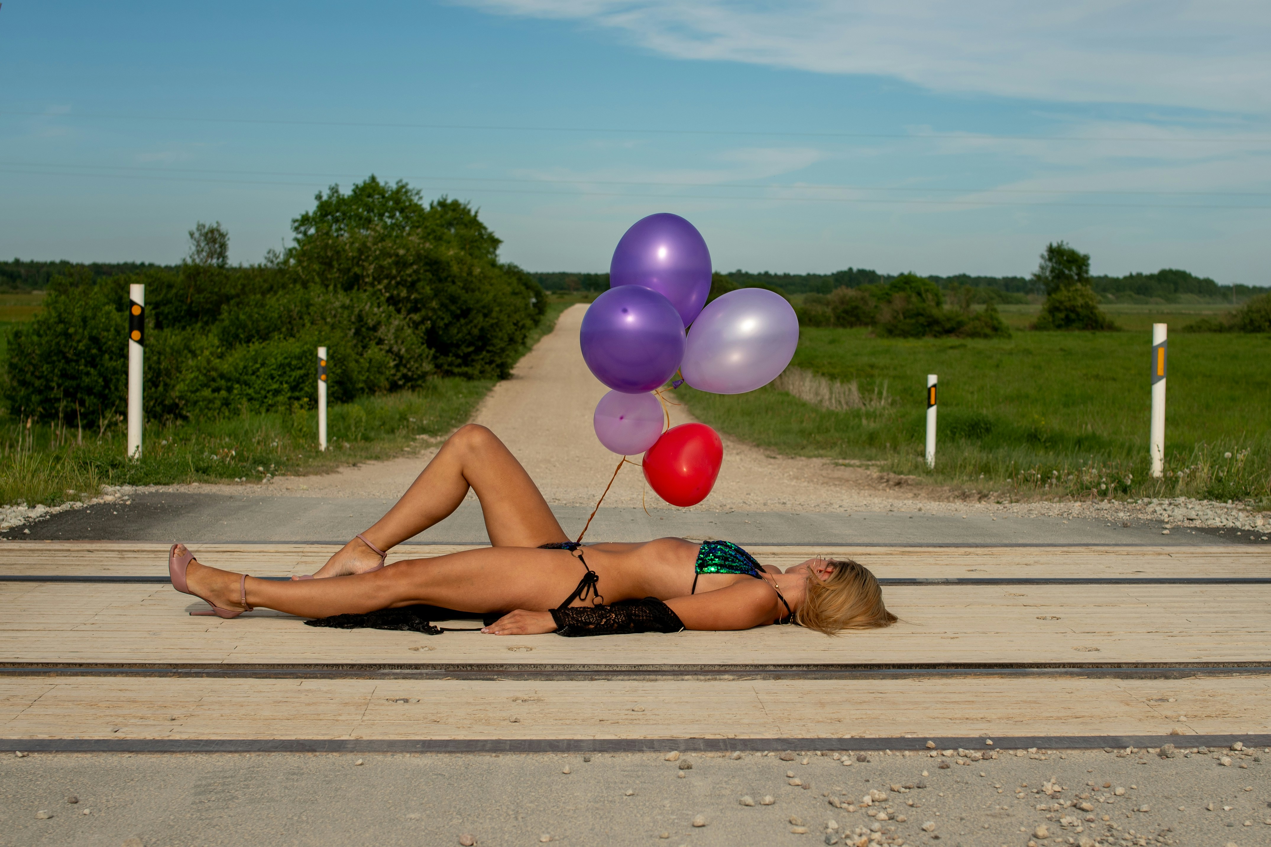 Wanita berbikini berbaring di rel kereta api dengan balon