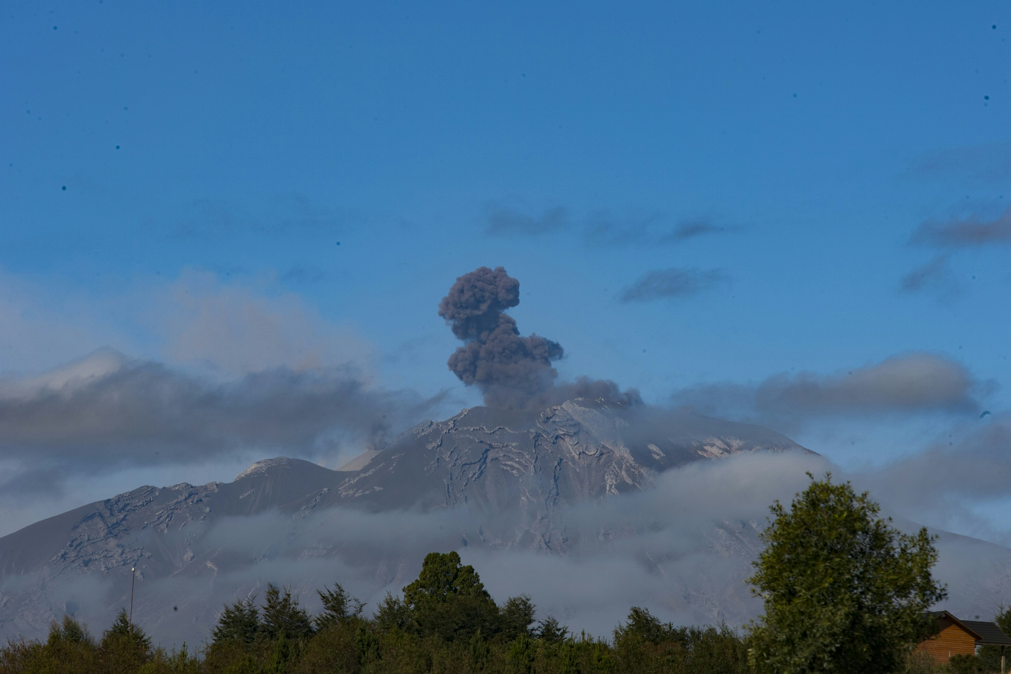 A volcano erupting, spewing ash into the blue sky