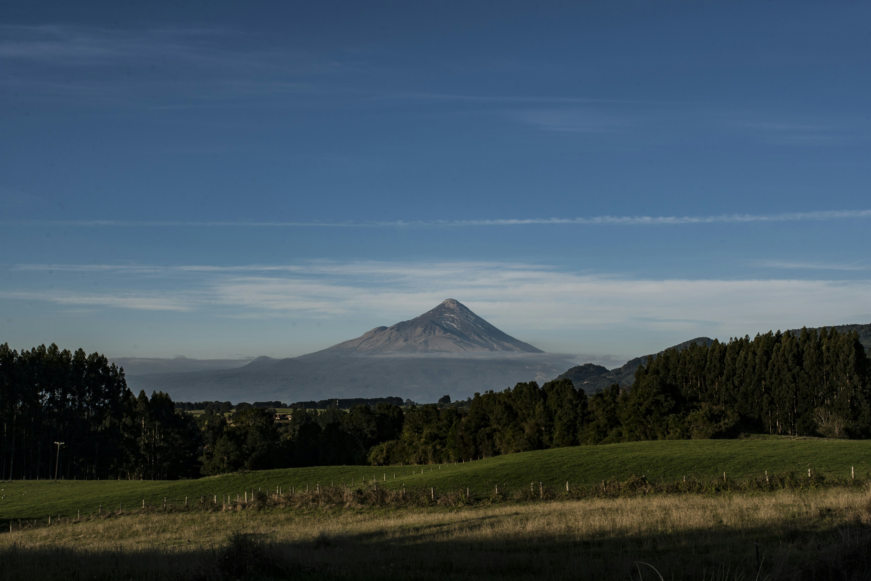 Cone-shaped mountain rises above green hills and blue sky