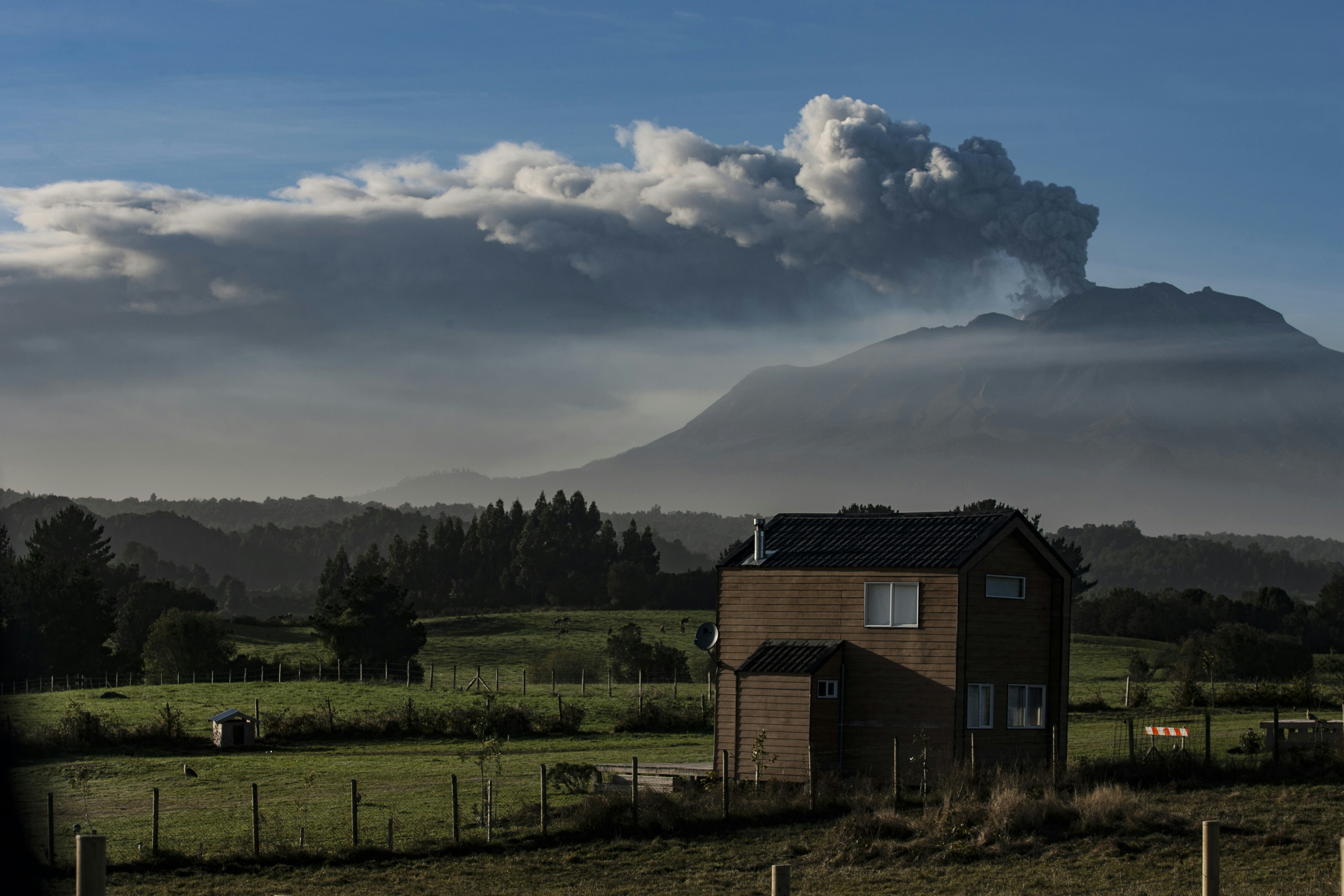 House in a field with a distant volcano erupting