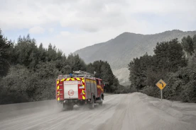 Fire truck drives on a dusty road near mountains.