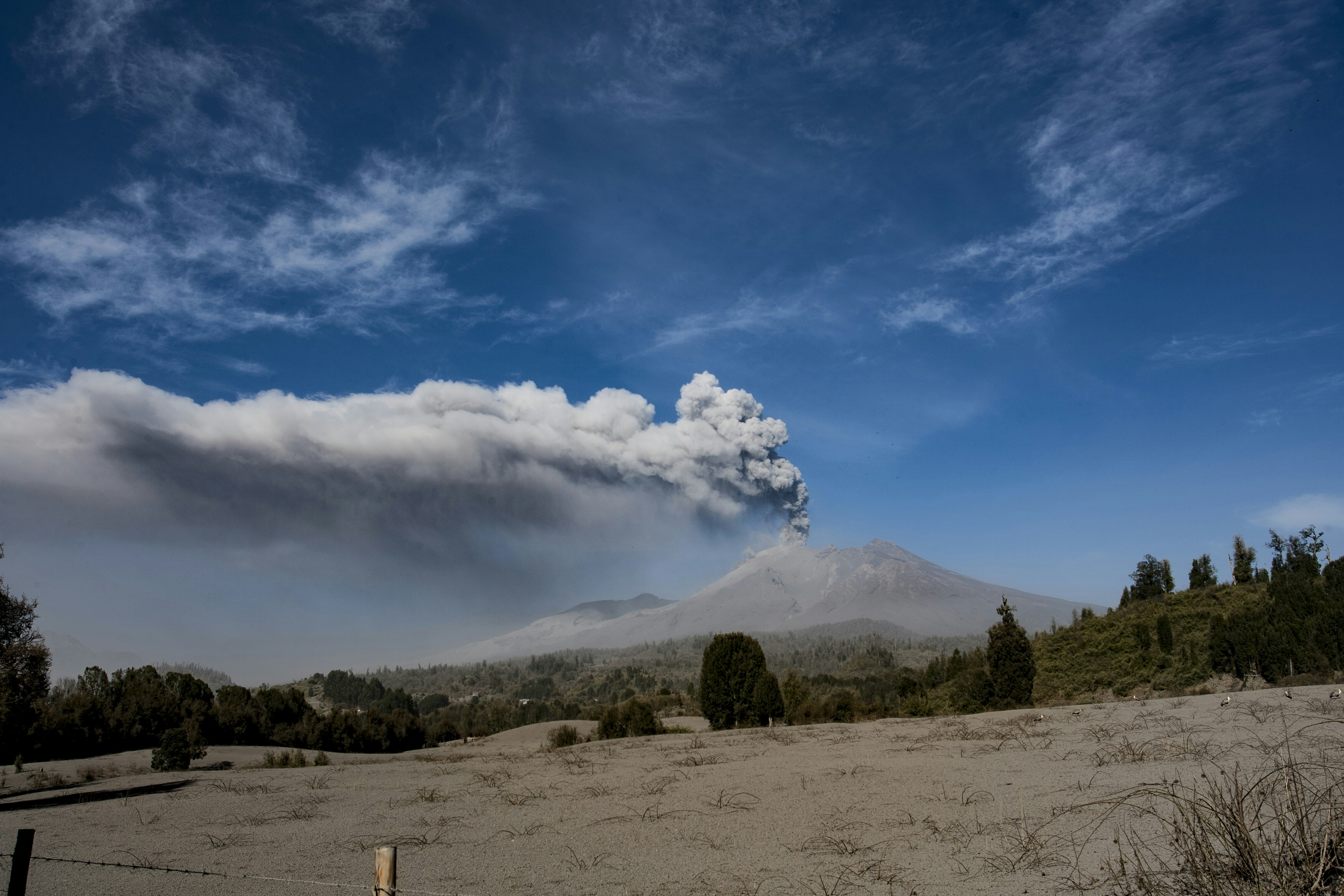Ash plume rises from erupting volcano under a blue sky