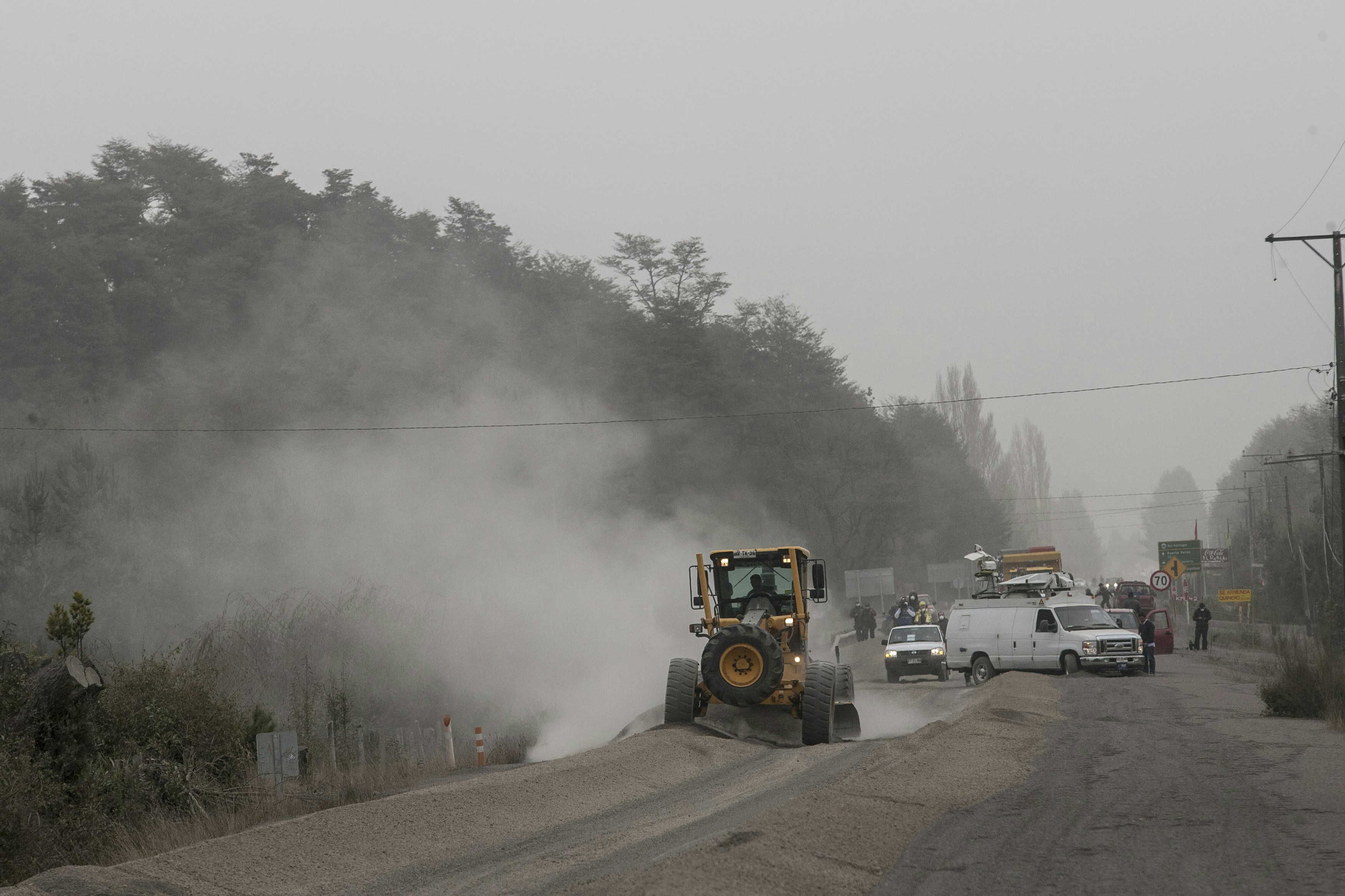 A bulldozer clears a dusty road under a hazy sky