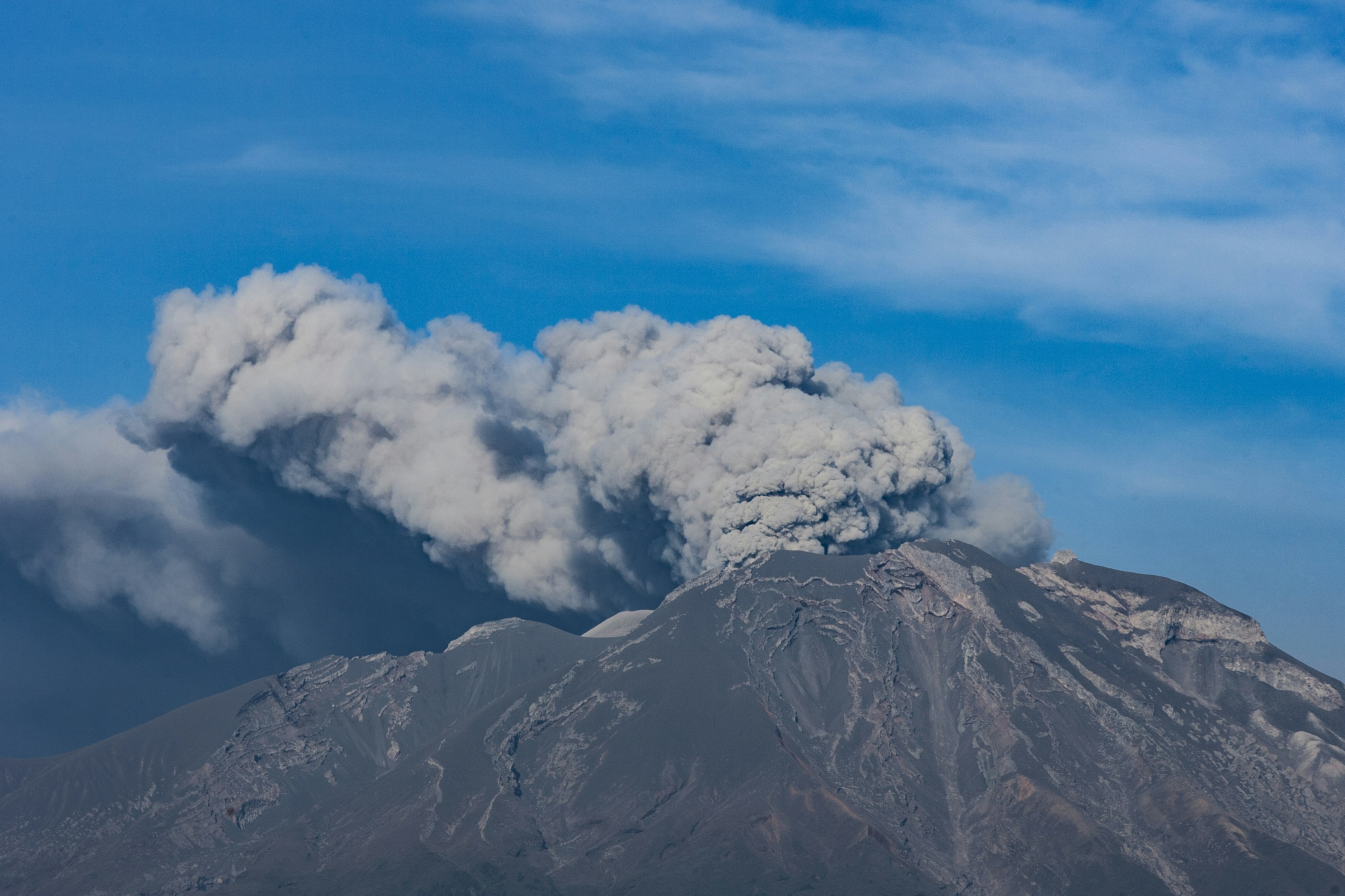 Volcano erupts, spewing ash and smoke into blue sky
