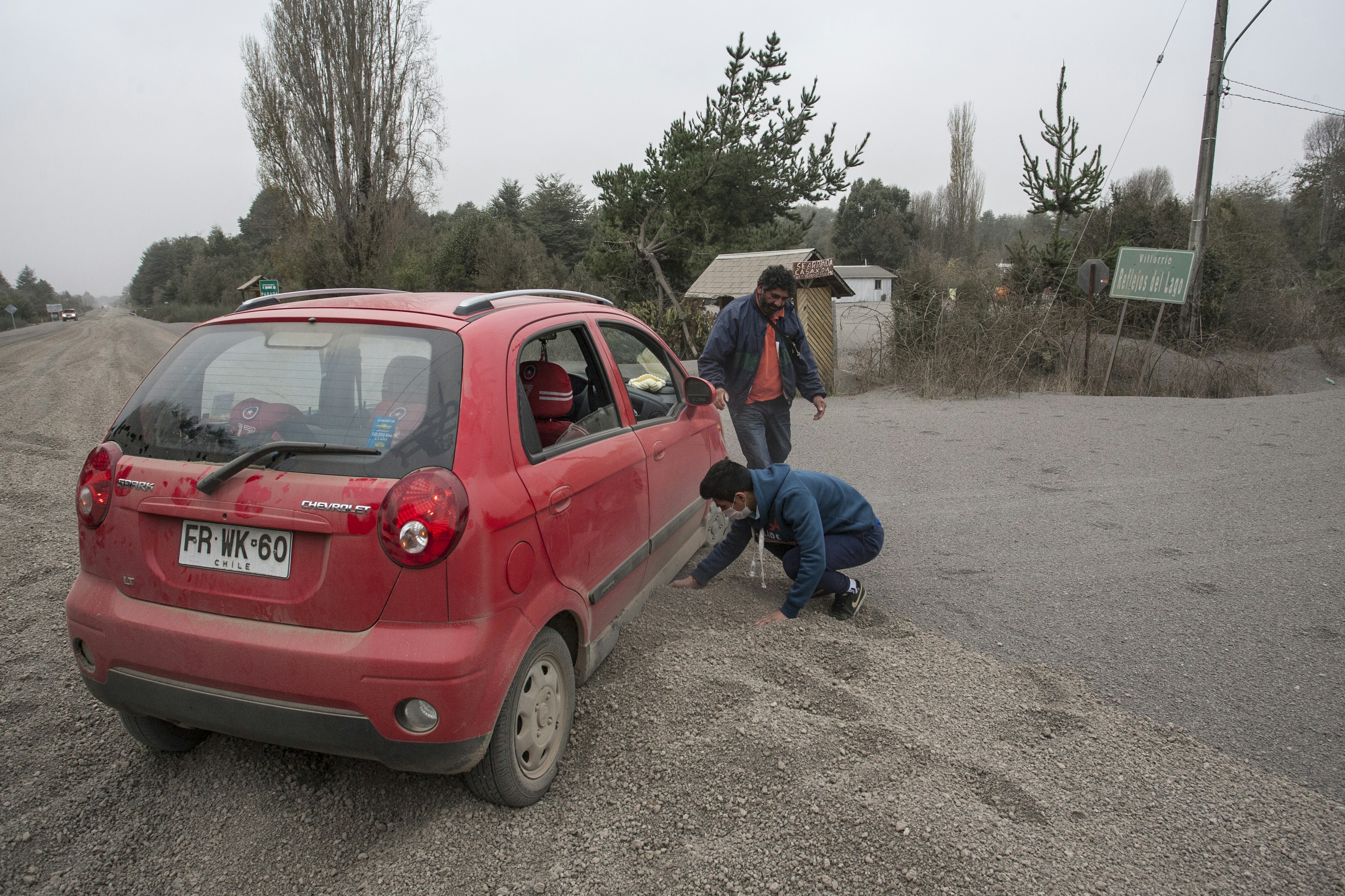 Two men helping a red car stuck in gravel