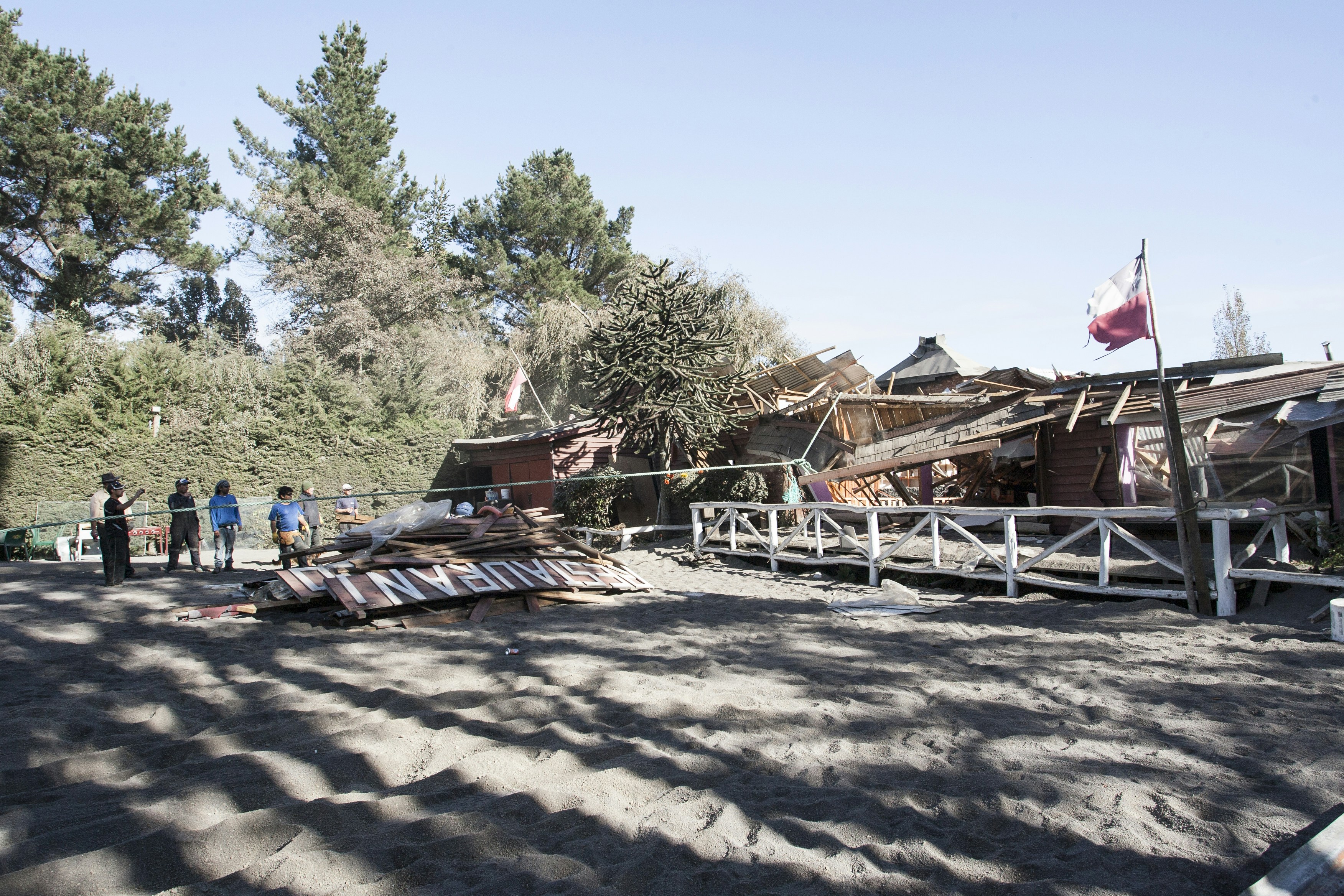 Damaged buildings and debris on sandy ground with people
