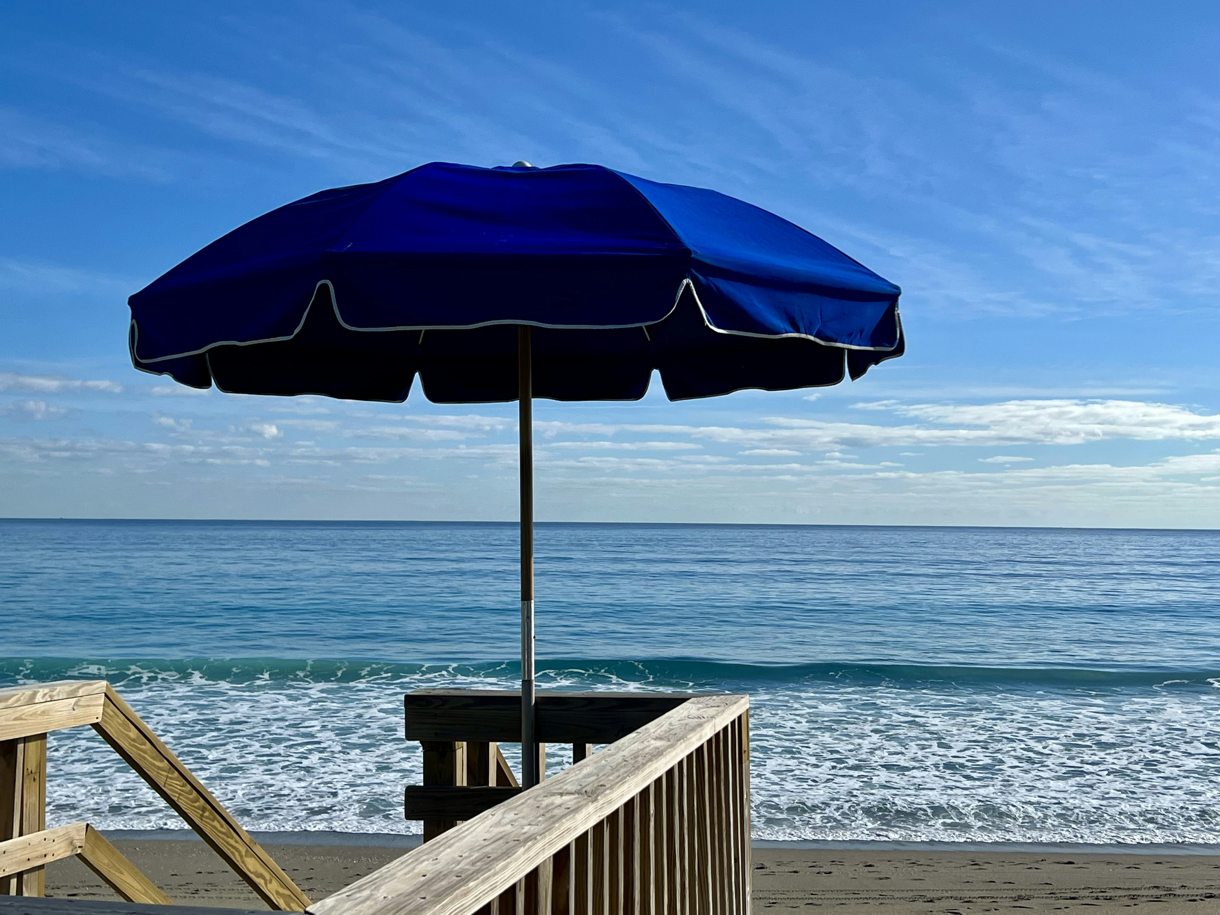Blue umbrella on a beach with ocean waves.