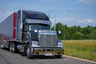 A black semi-truck drives down a rural road.
