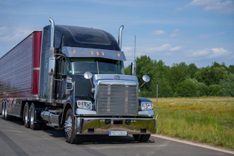 A black semi-truck drives down a rural road.