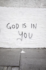 White brick wall with "god is in you" graffiti.