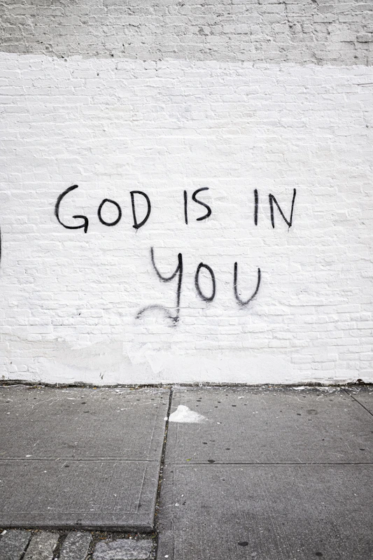 White brick wall with "god is in you" graffiti.