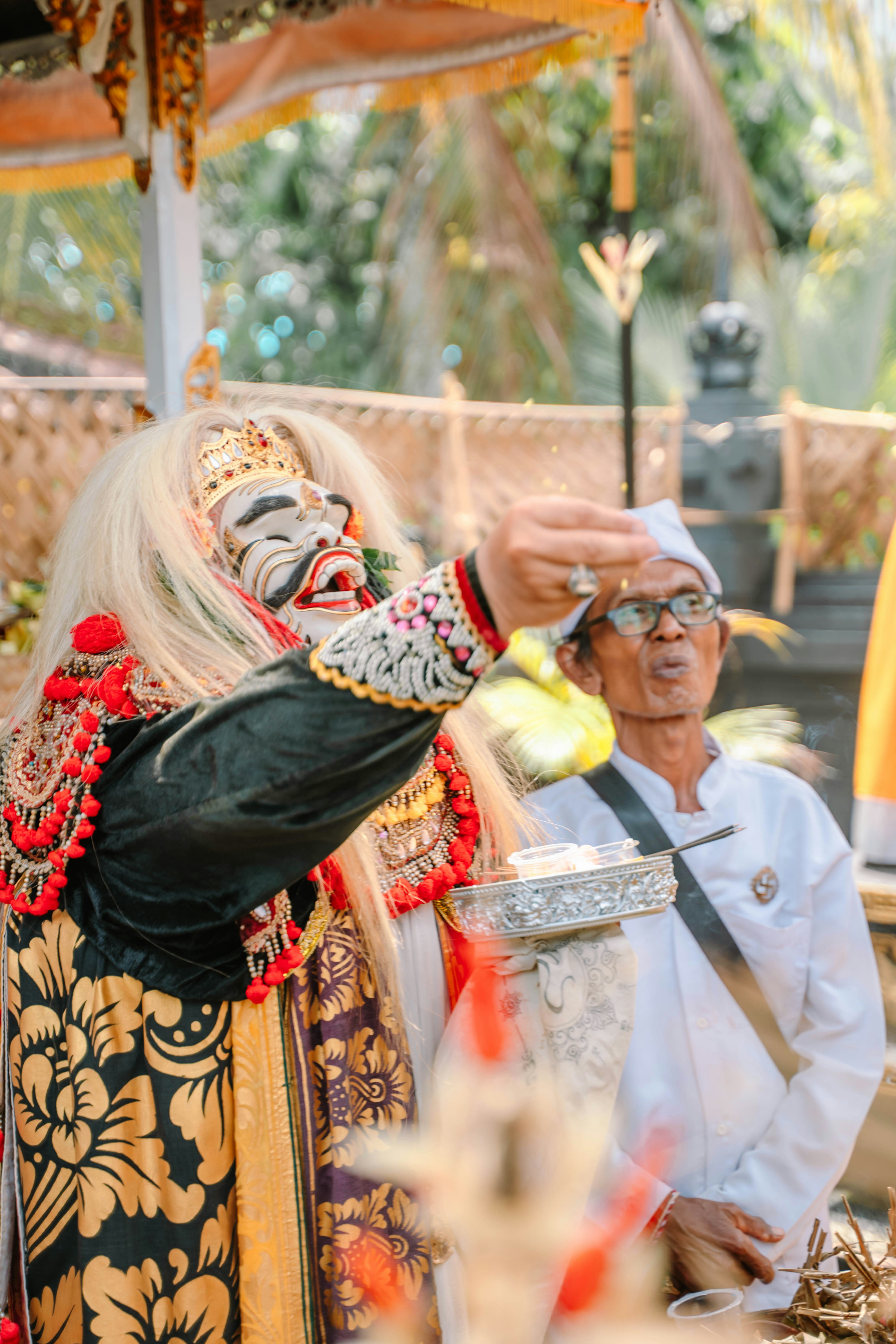 A performer in a traditional mask and costume sprinkles offerings.
