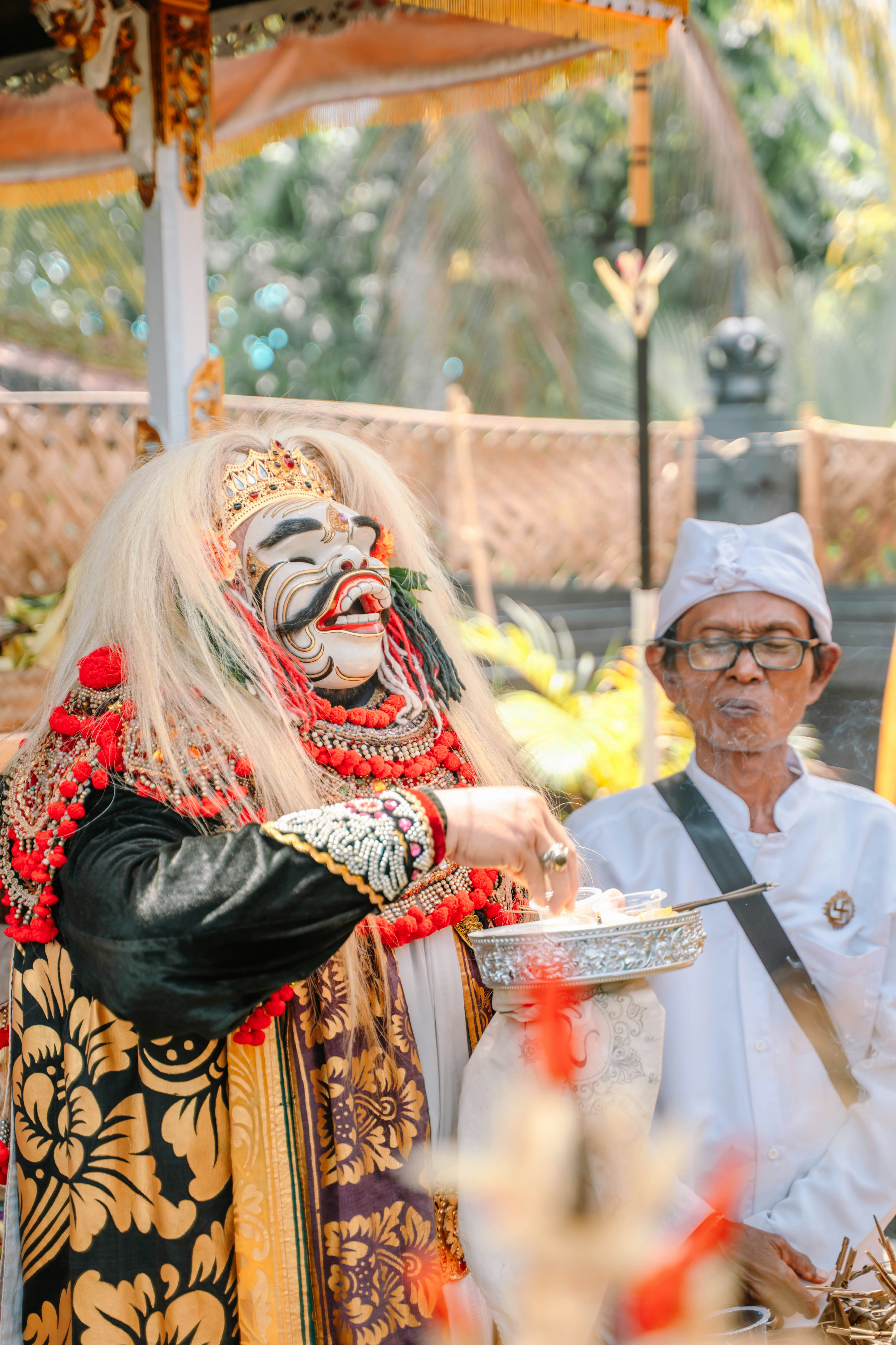 A person in a traditional mask and costume offers food.