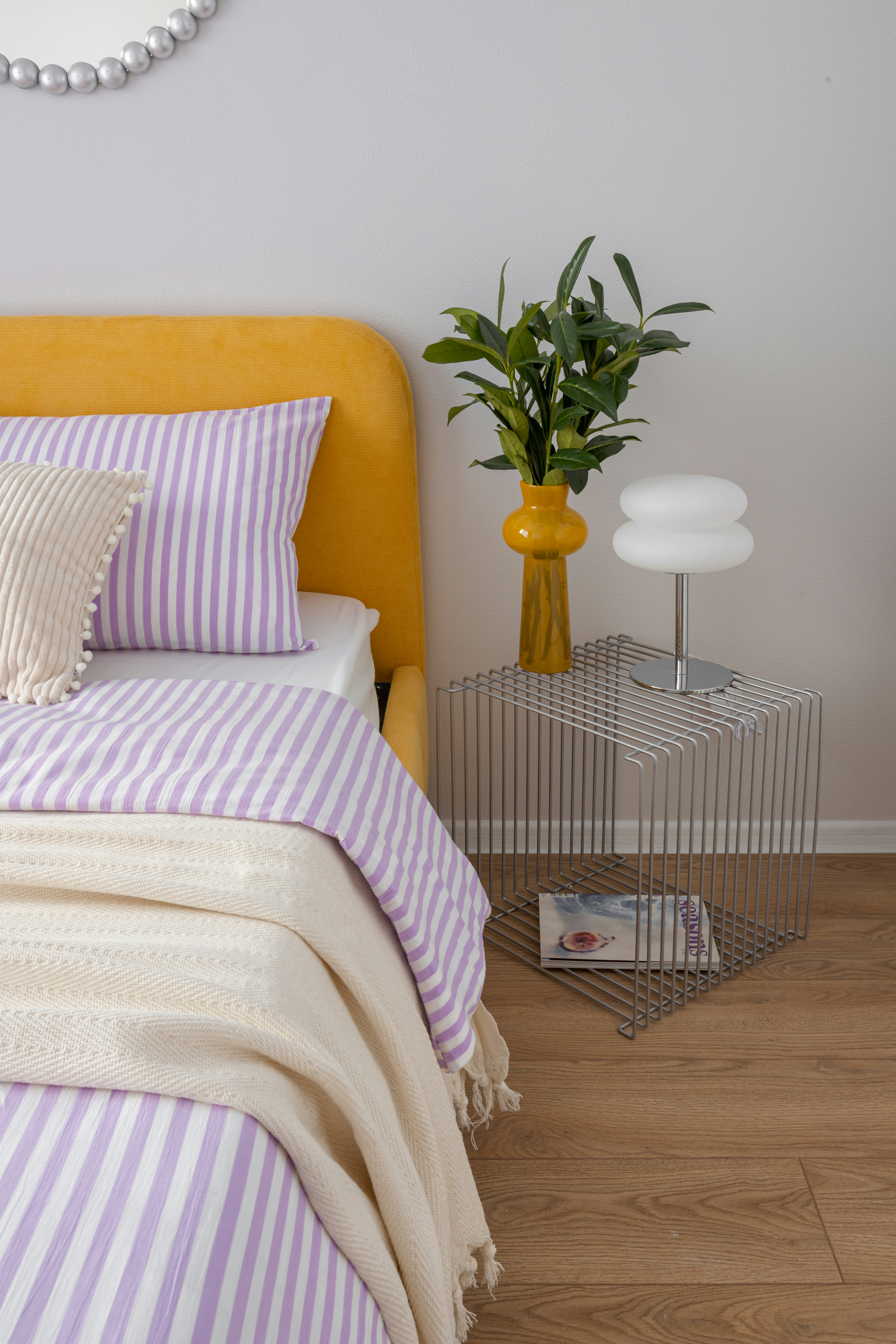 A yellow headboard with striped bedding and a cream blanket.