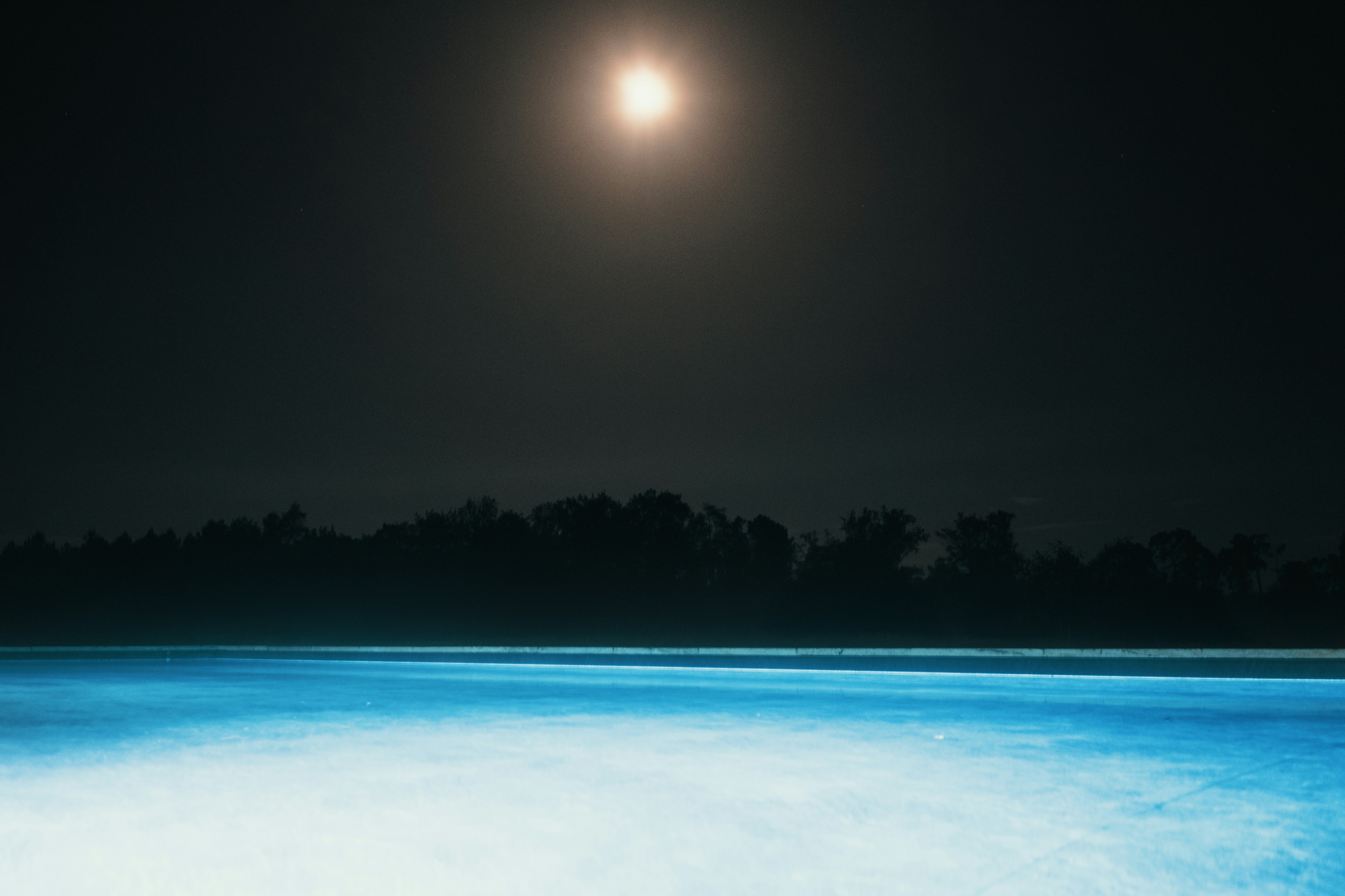 Noite iluminada pela lua sobre uma piscina azul brilhante