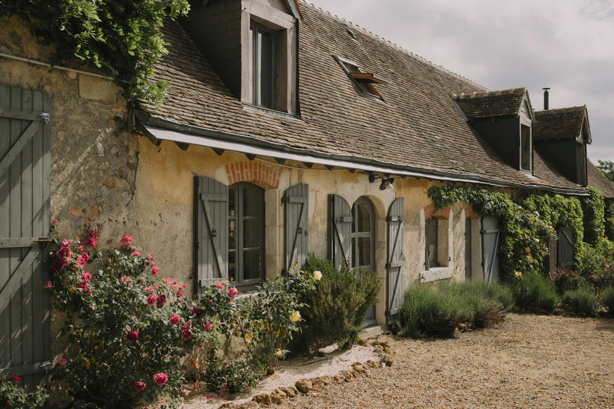 Façade en pierre du Domaine de la Vienne avec roses et volets à Civaux