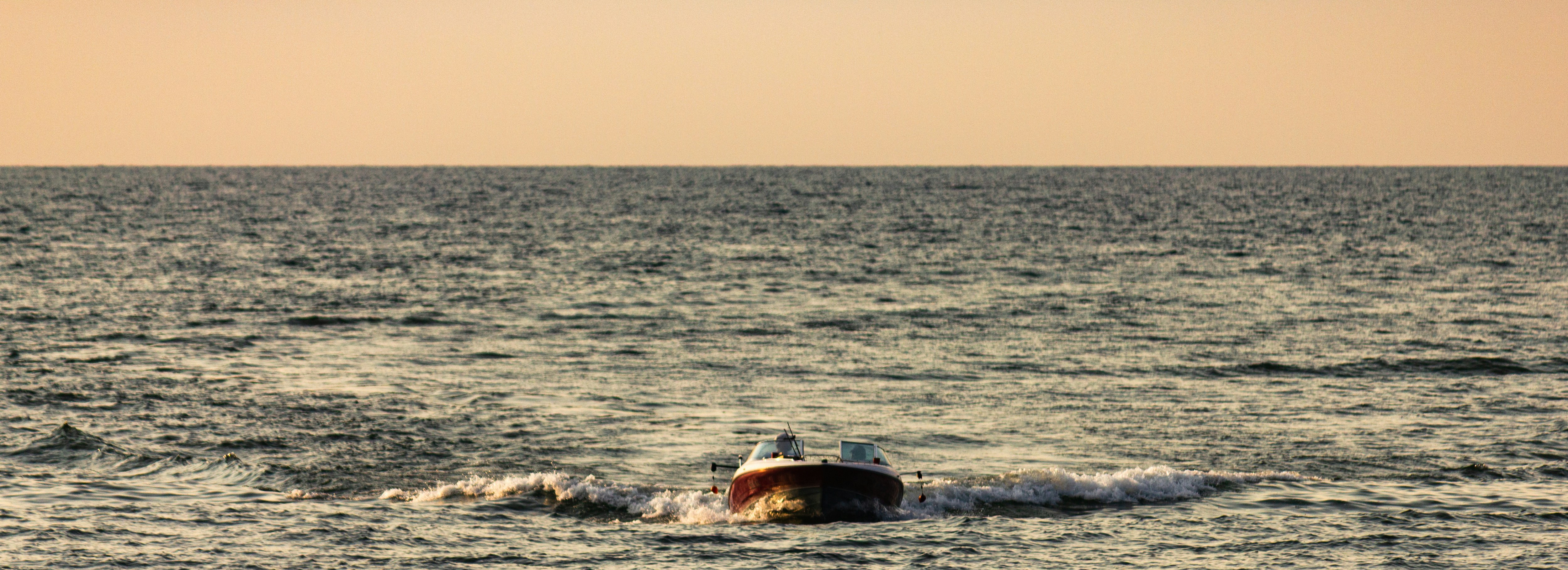 Un petit bateau traverse l’océan agité au coucher du soleil.