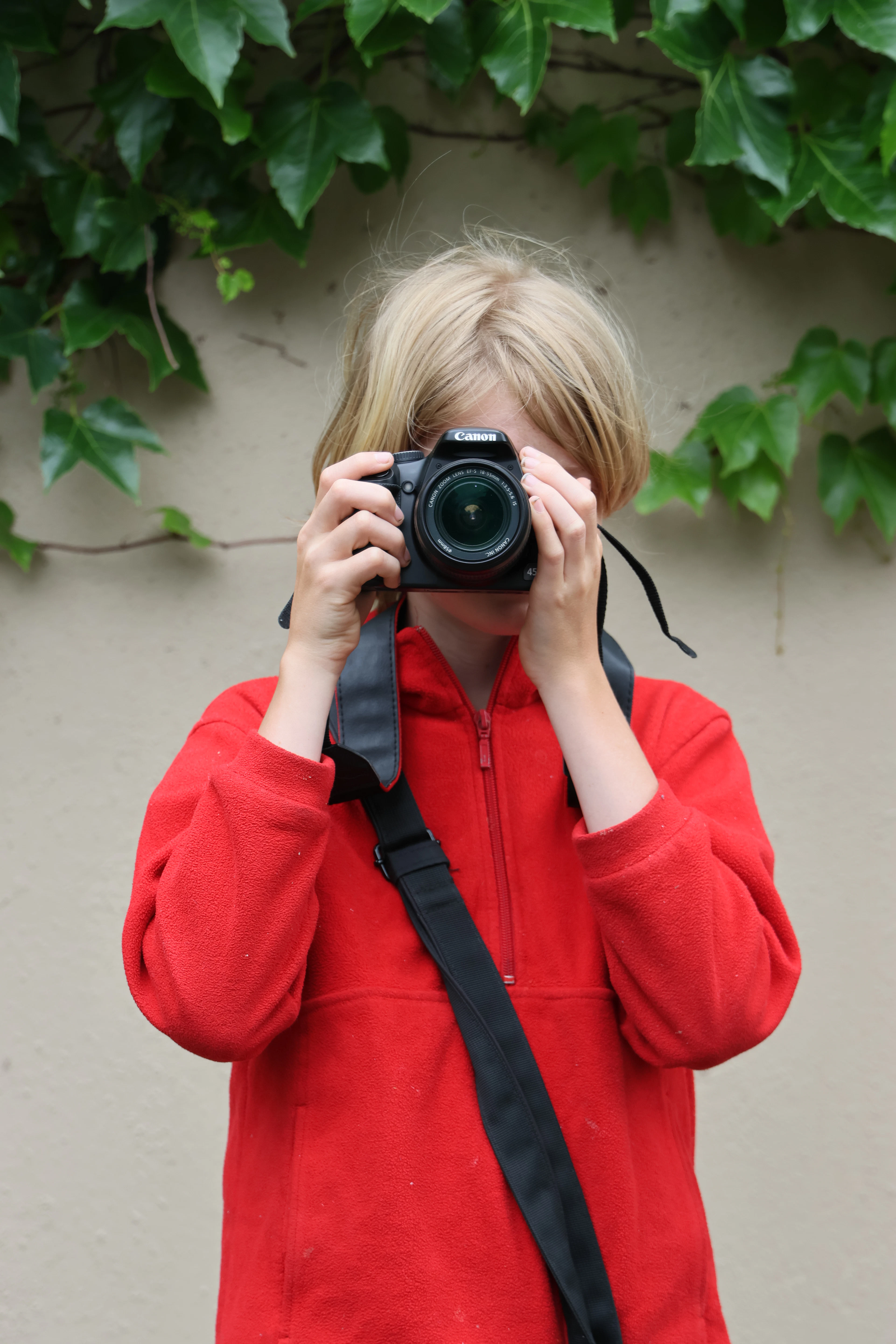 A child in a red hoodie taking a photo with a camera
