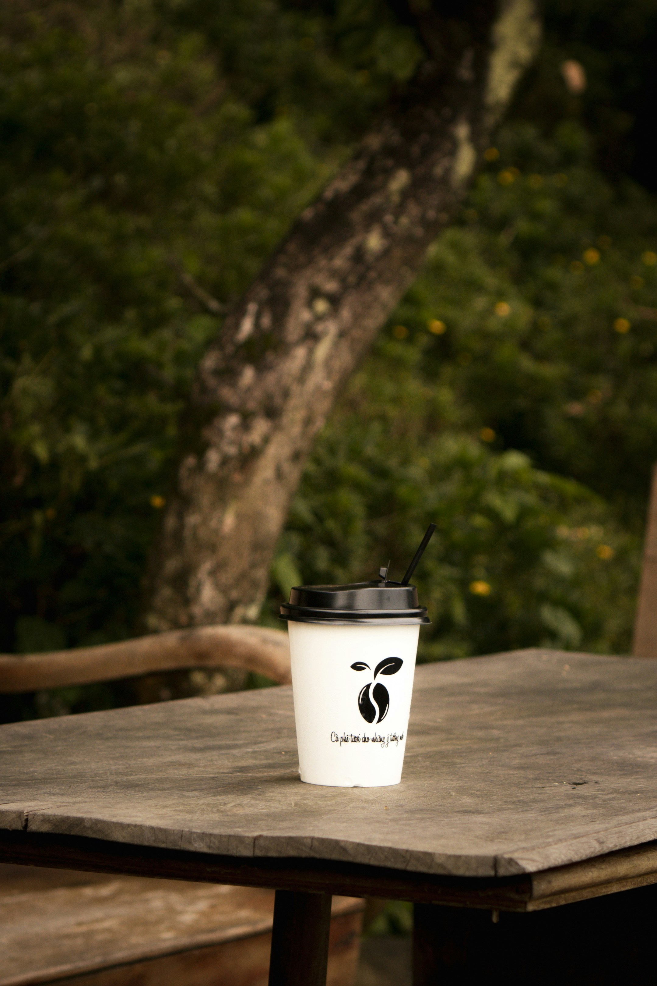 Cangkir kopi dengan logo di atas meja kayu pedesaan.