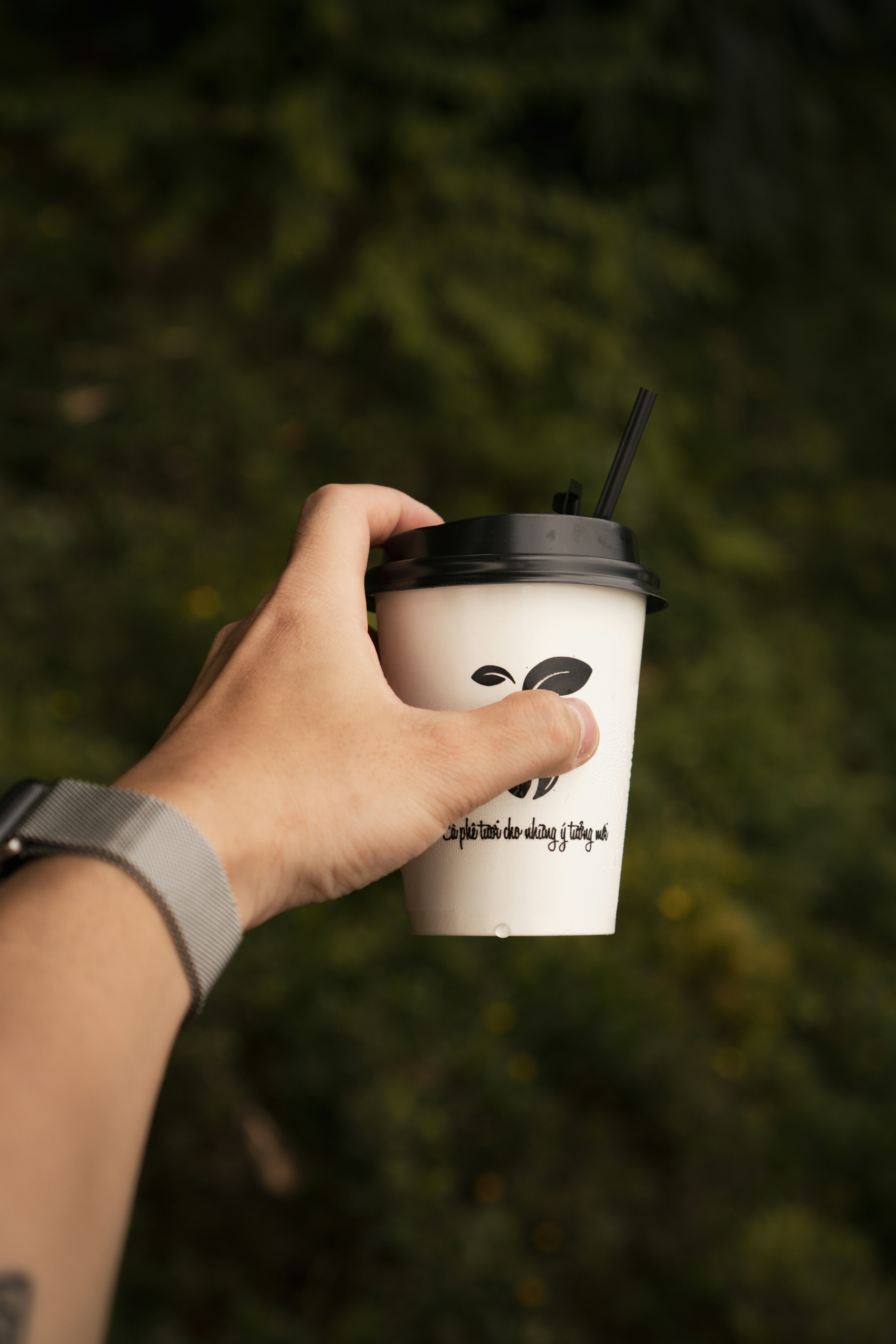 Tangan memegang cangkir kopi sekali pakai dengan sedotan.