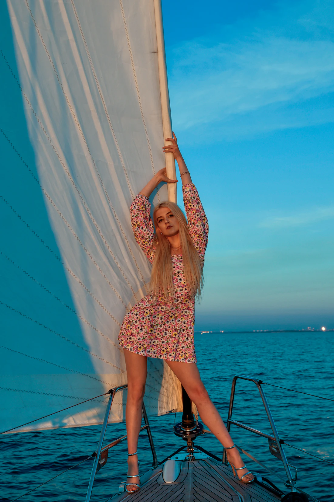 Model in a pink floral dress beside a white sail against a turquoise sky