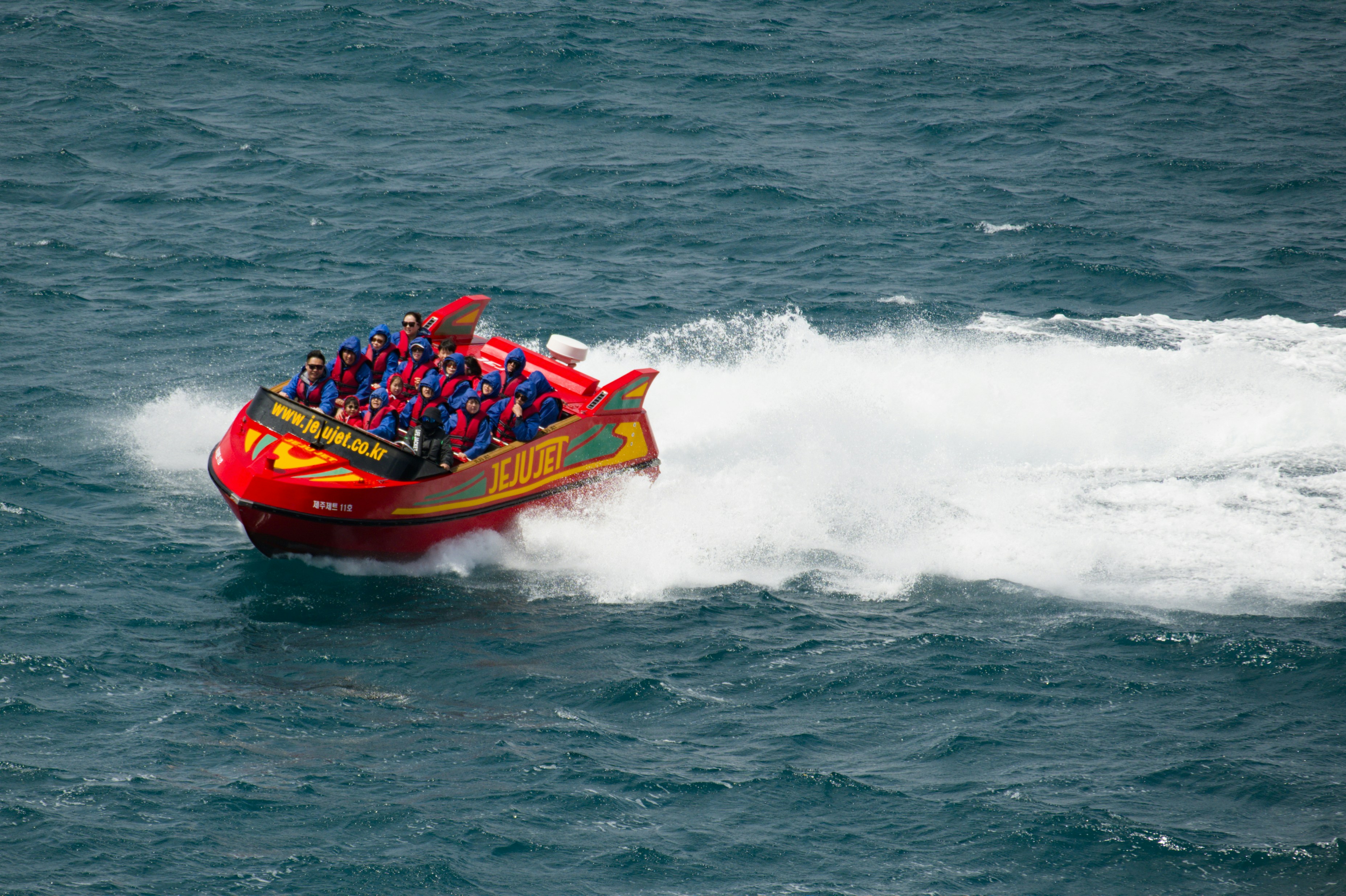 A red boat full of people speeds through the ocean.