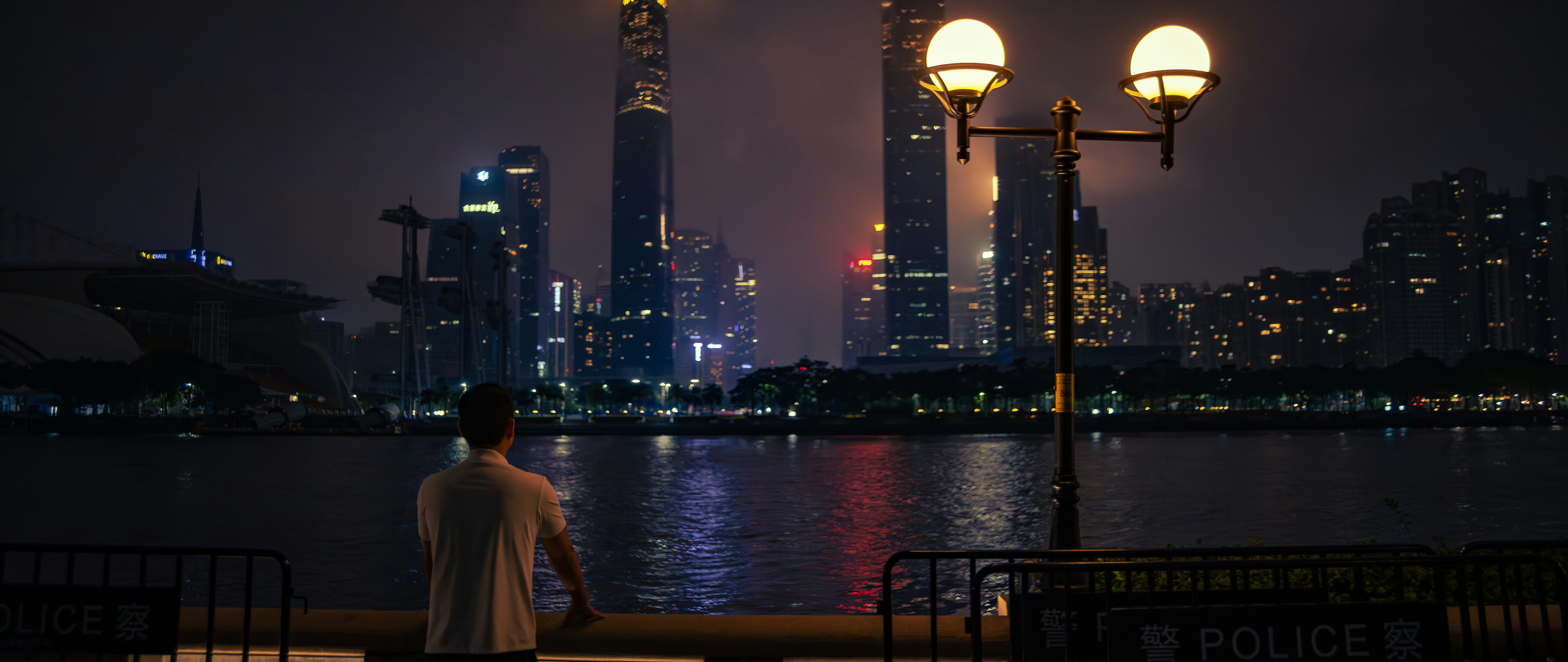 Man gazes at illuminated cityscape across water at night