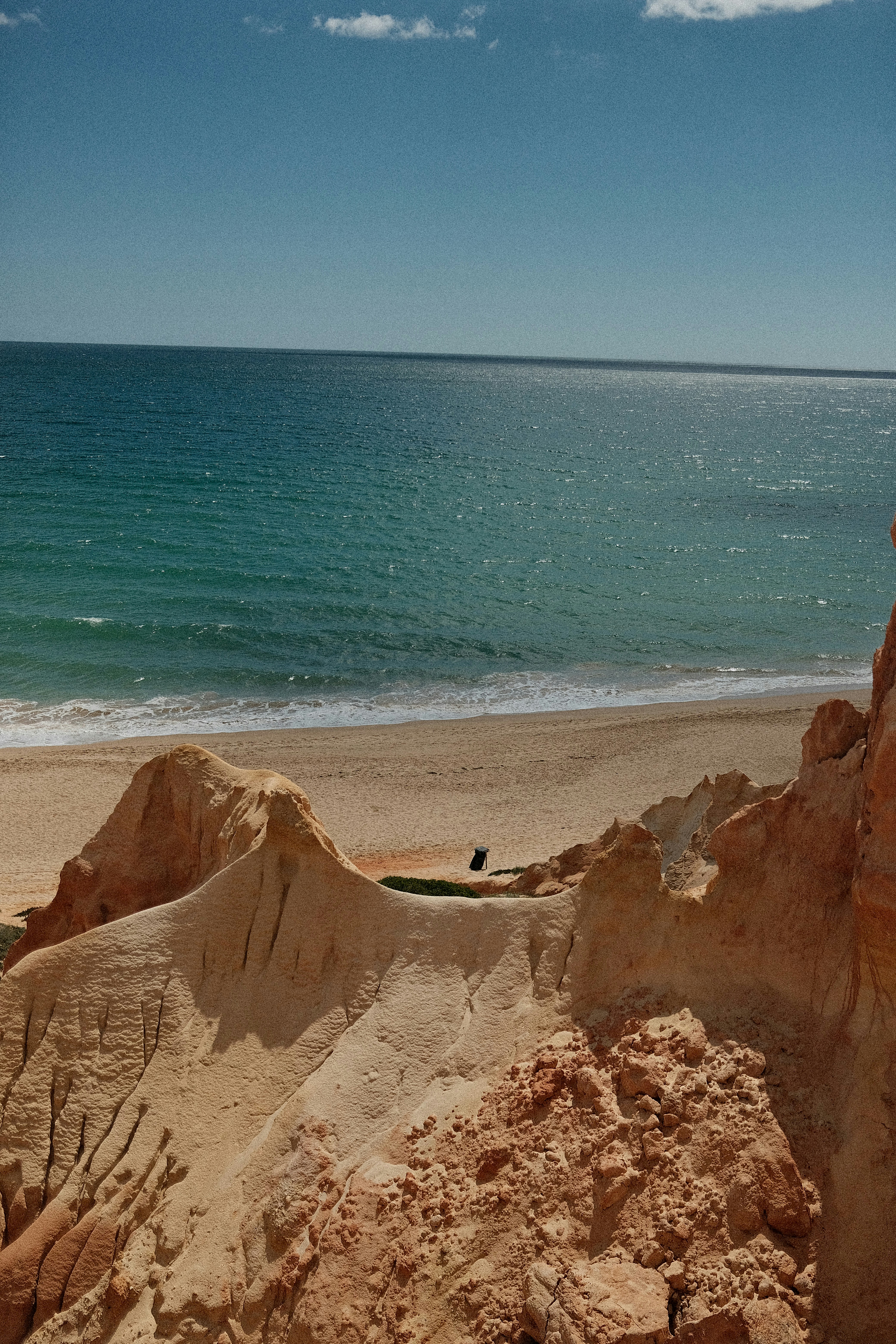 Sandy cliffs overlook a tranquil turquoise ocean and beach.