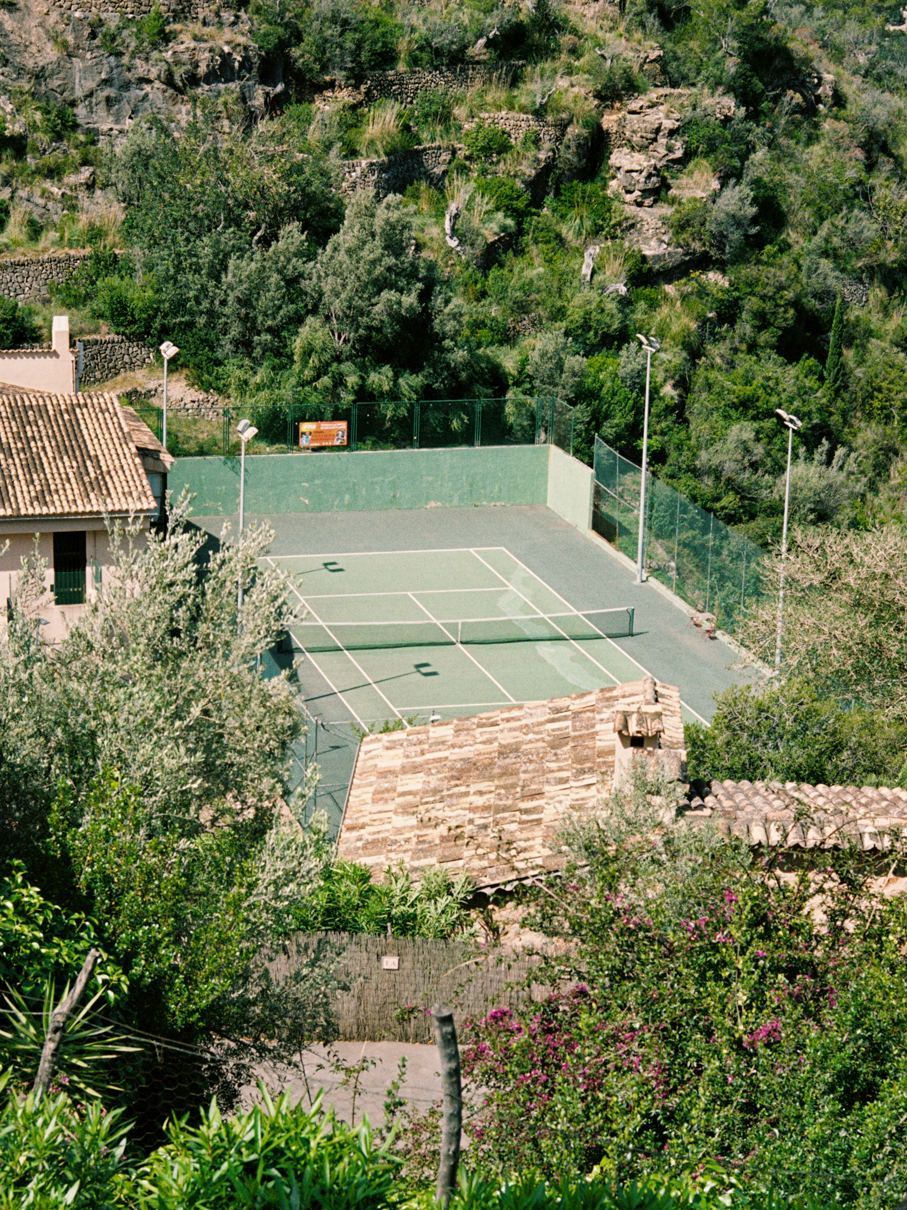 Tennis court nestled among lush green trees and buildings.