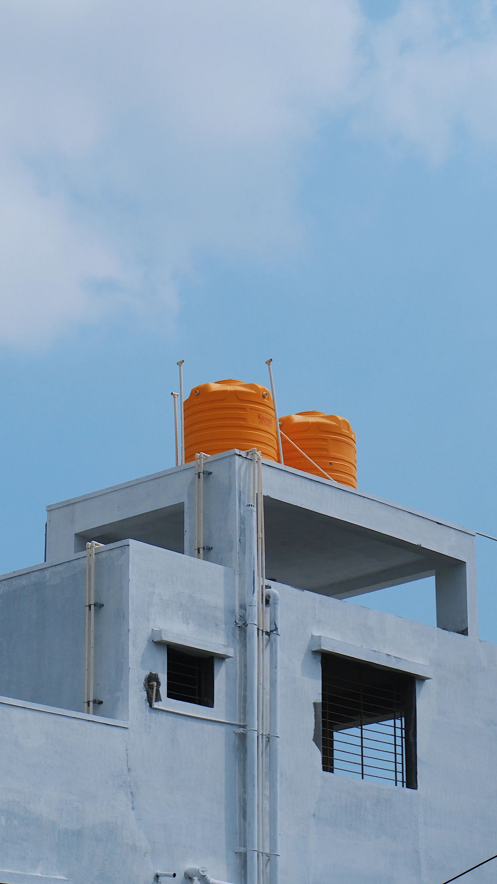 Two orange rooftop water storage tanks mounted on top of a building against a clear blue sky