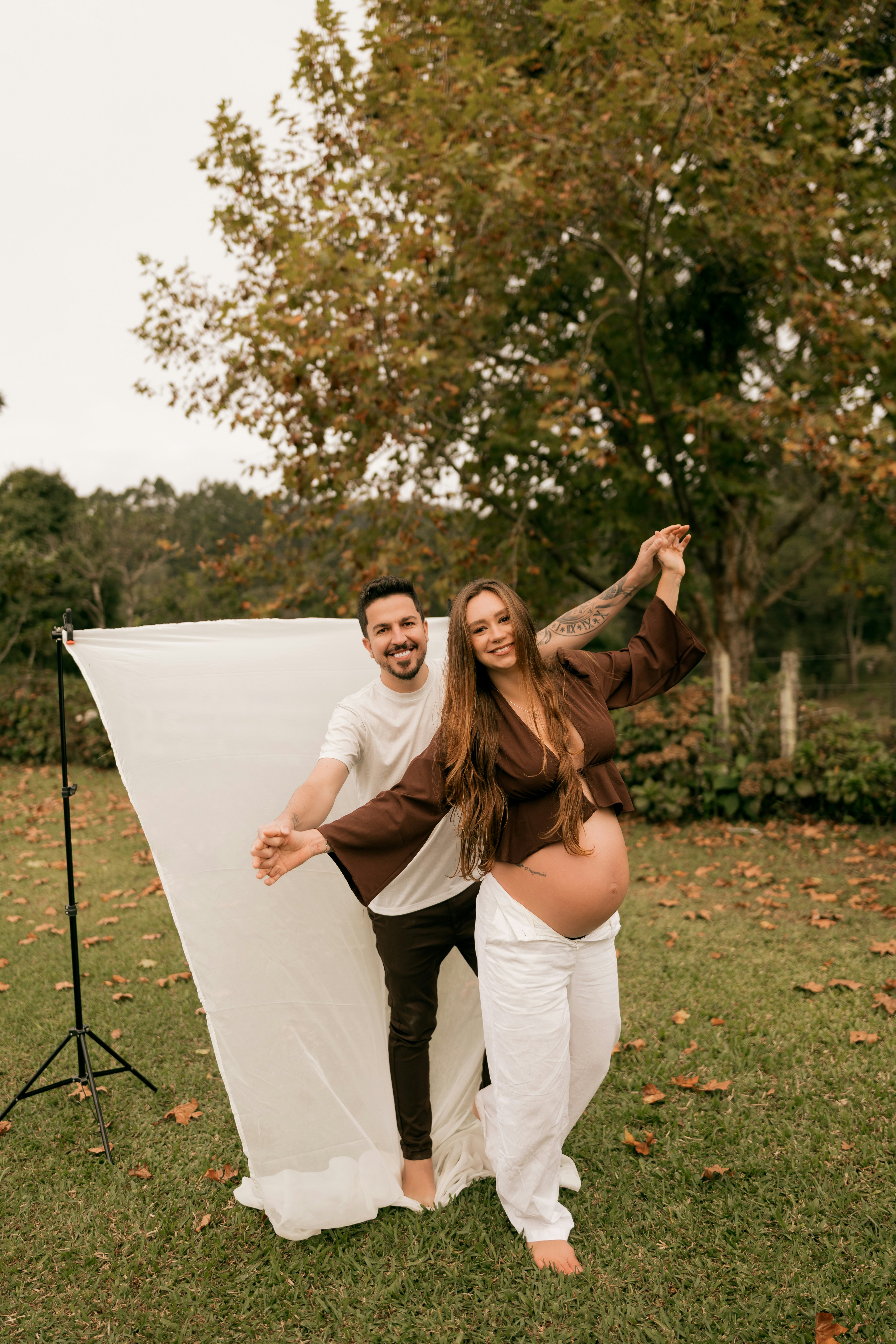 白い布と秋の落ち葉を手に屋外でポーズをとるカップル