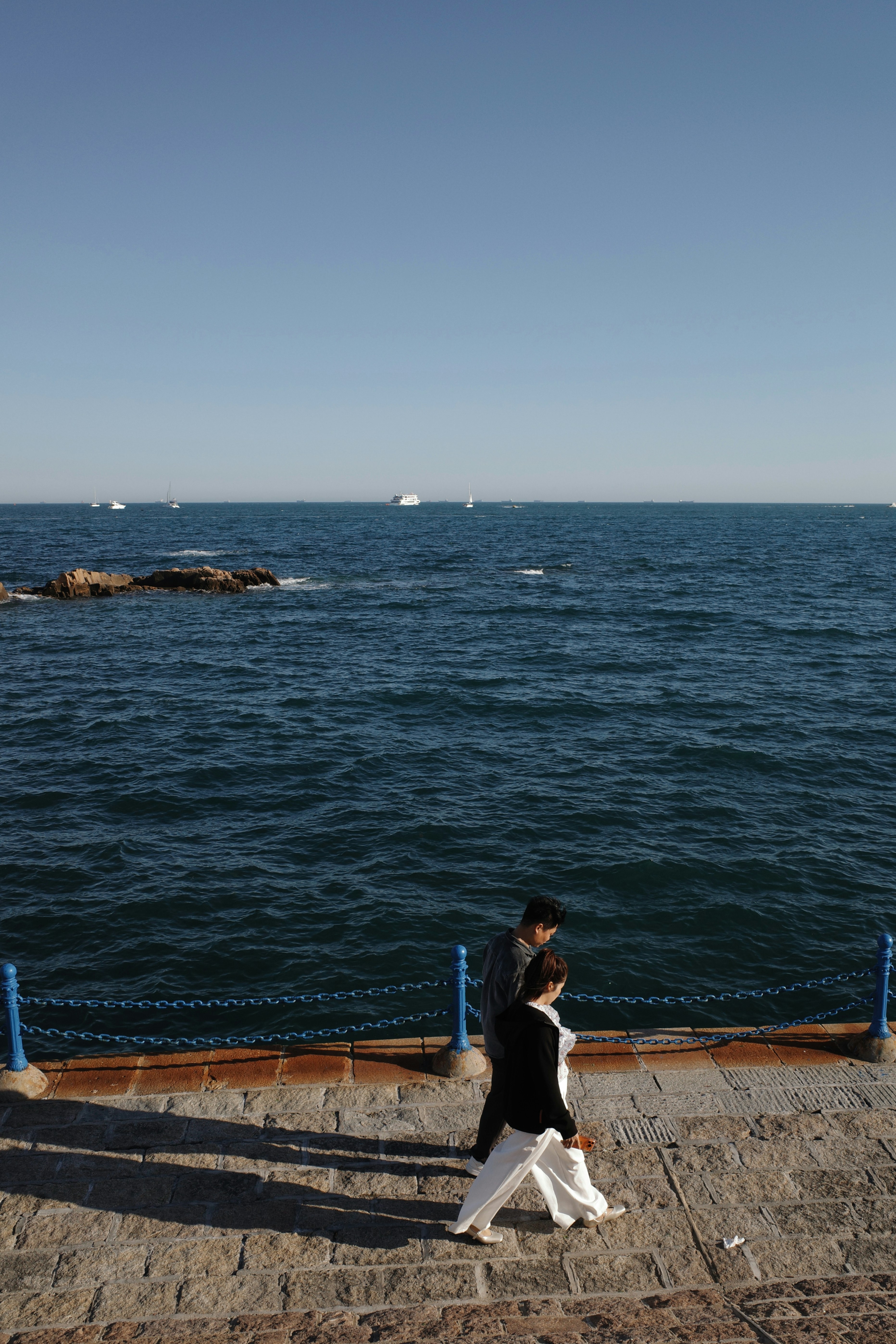 Two people walk along a stone path by the ocean.