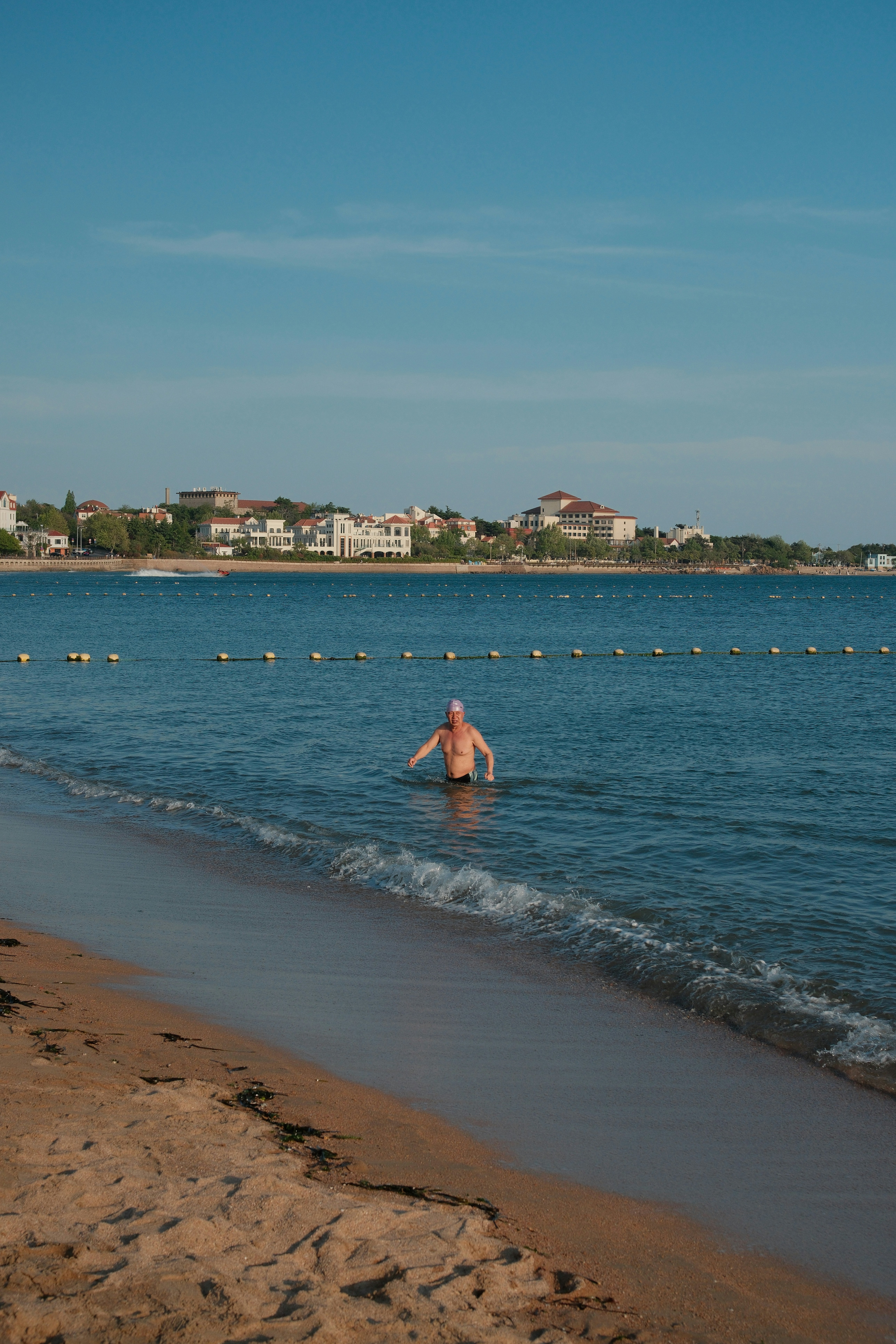 Man wading into the ocean near a sandy beach.