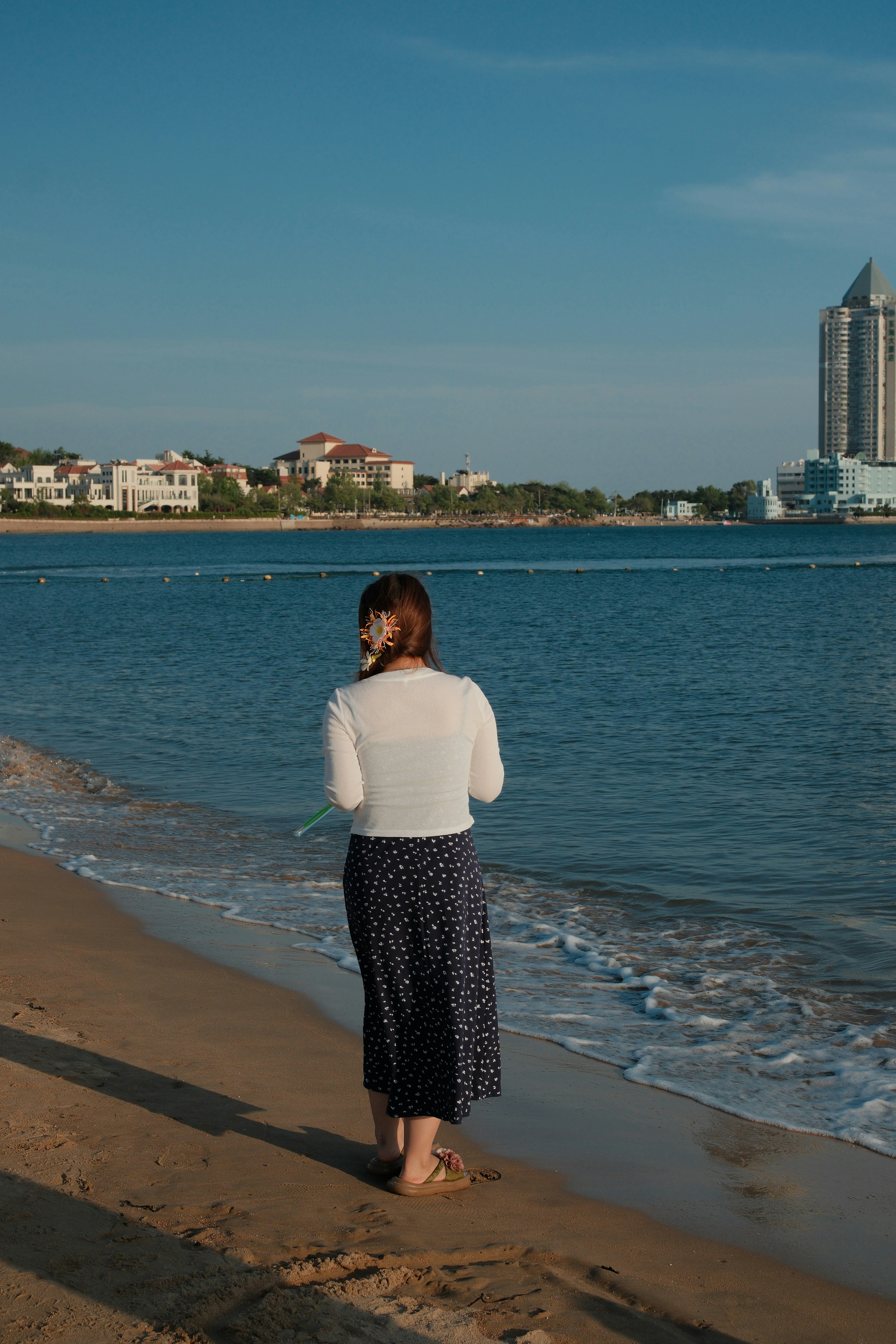A woman stands on a sandy beach by the ocean.