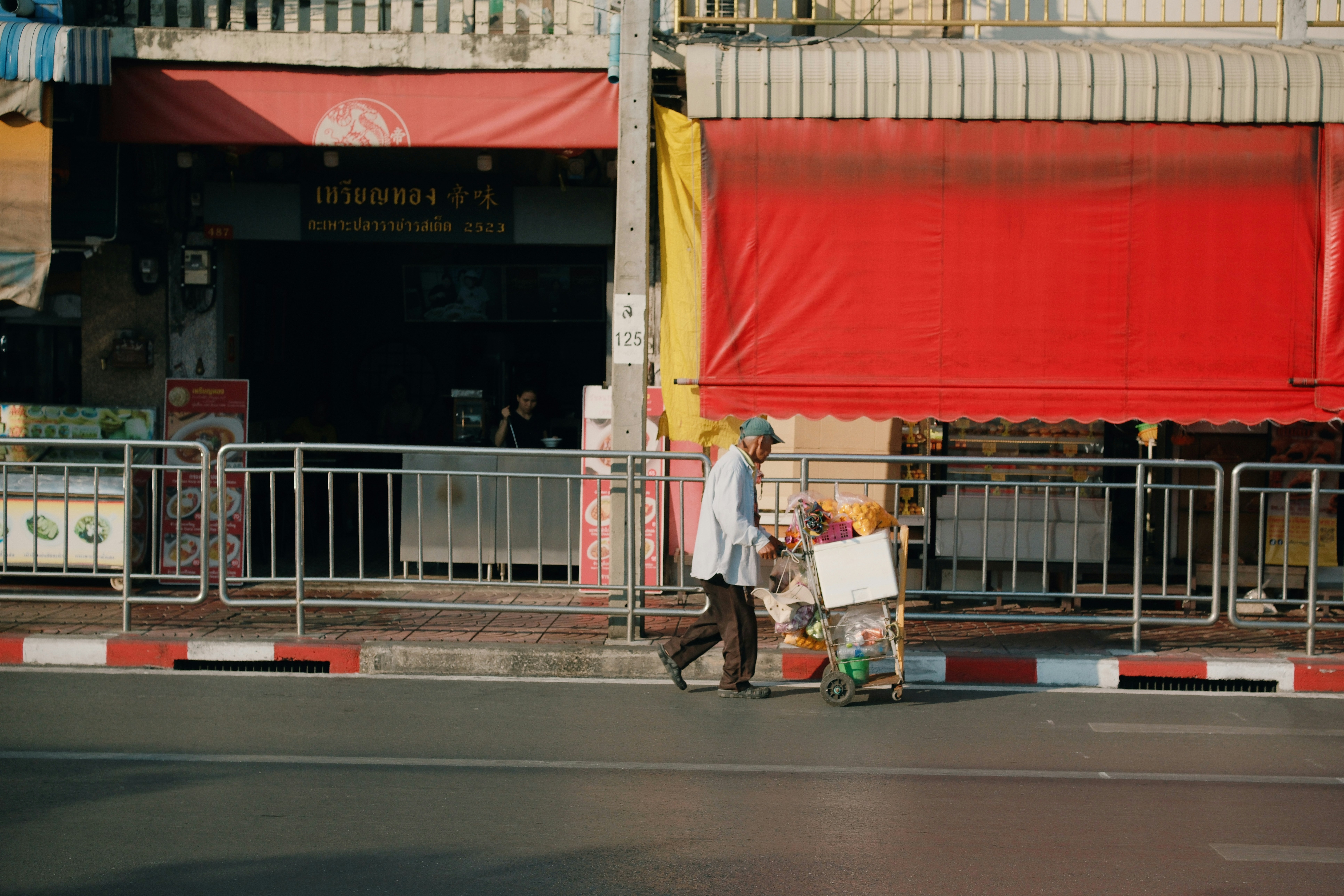 Man pushing cart along a street with red awnings.