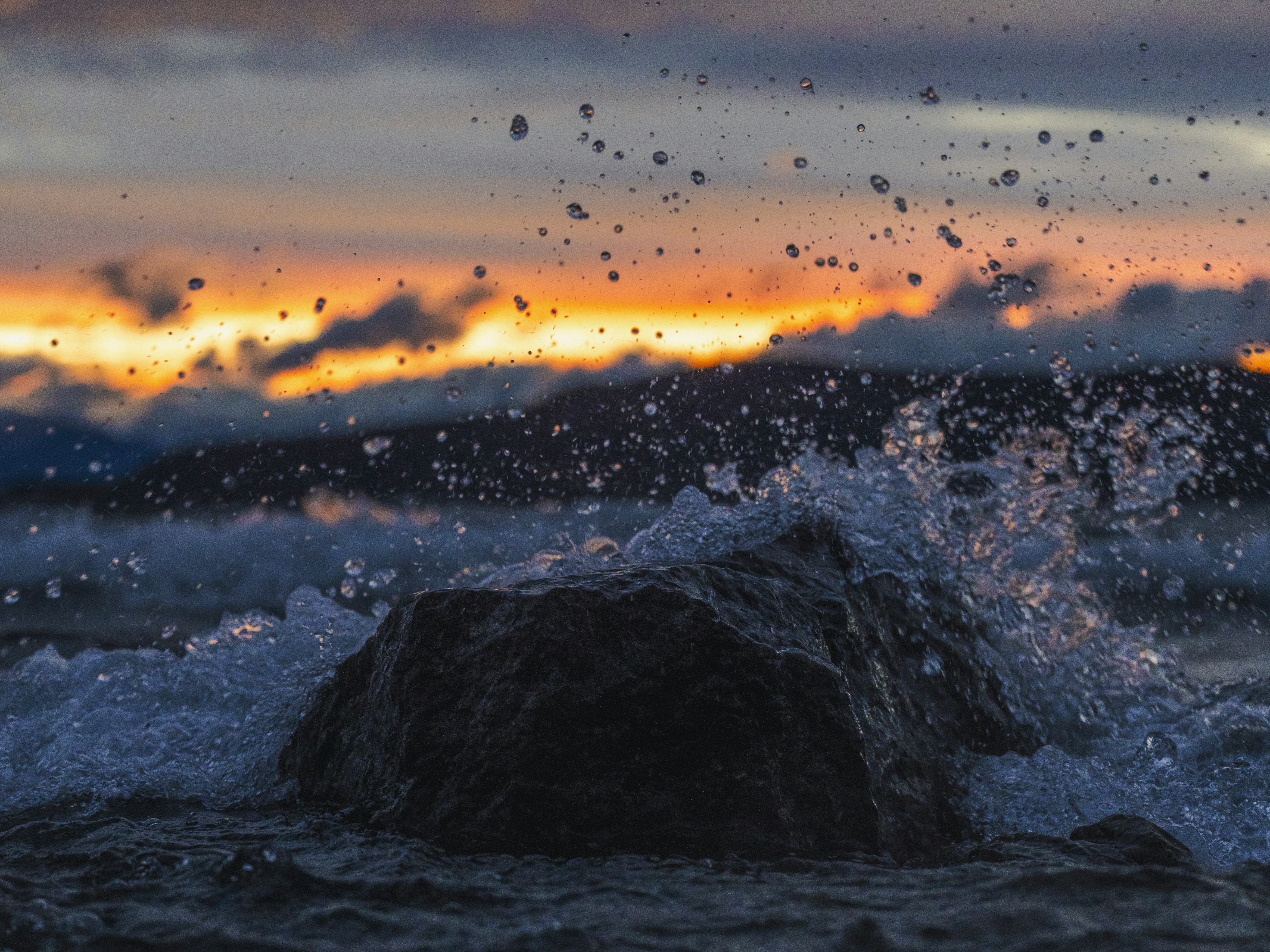 Waves crashing against a rock at sunset