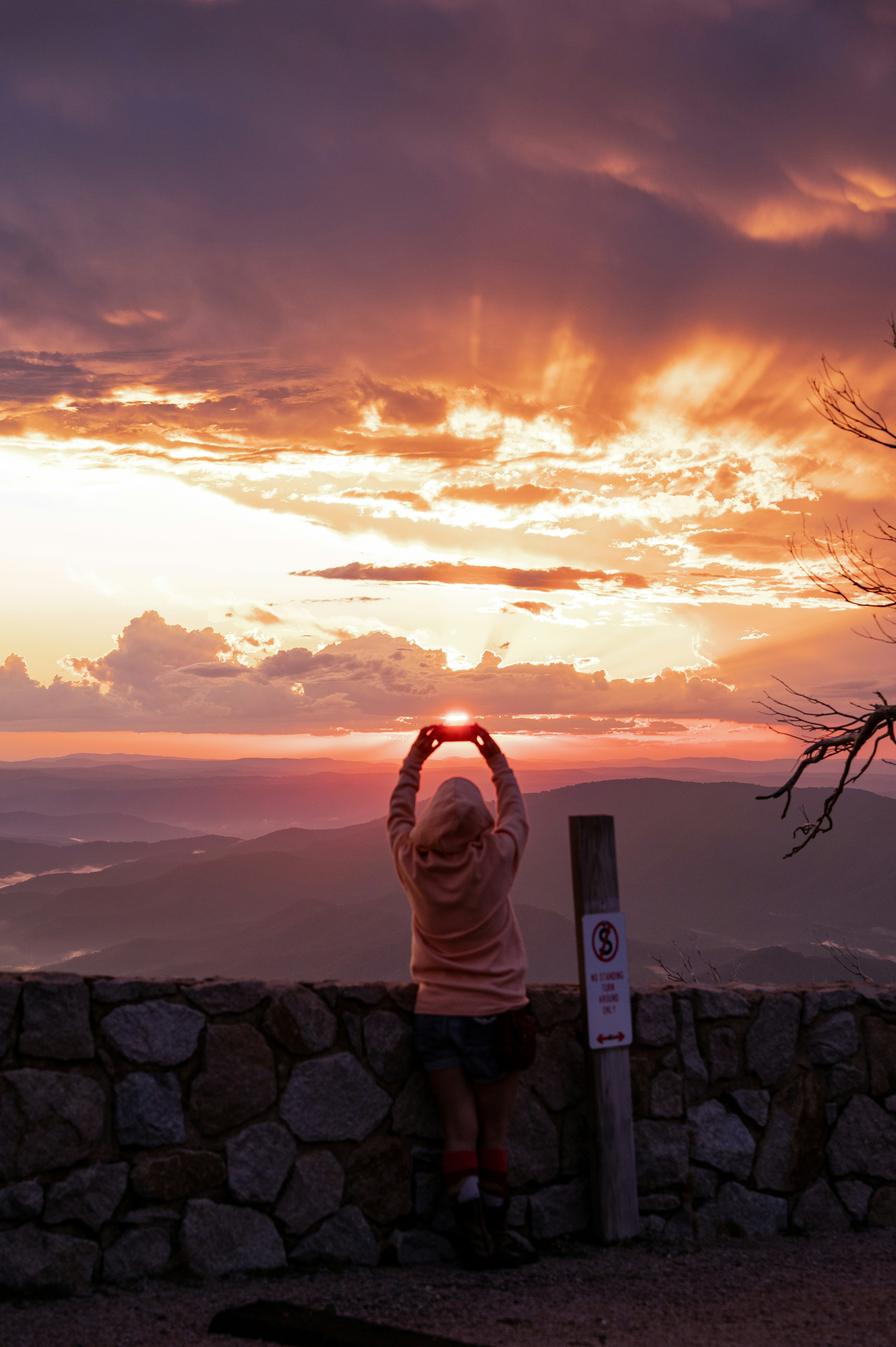 Person holding the sun at sunset over mountains.