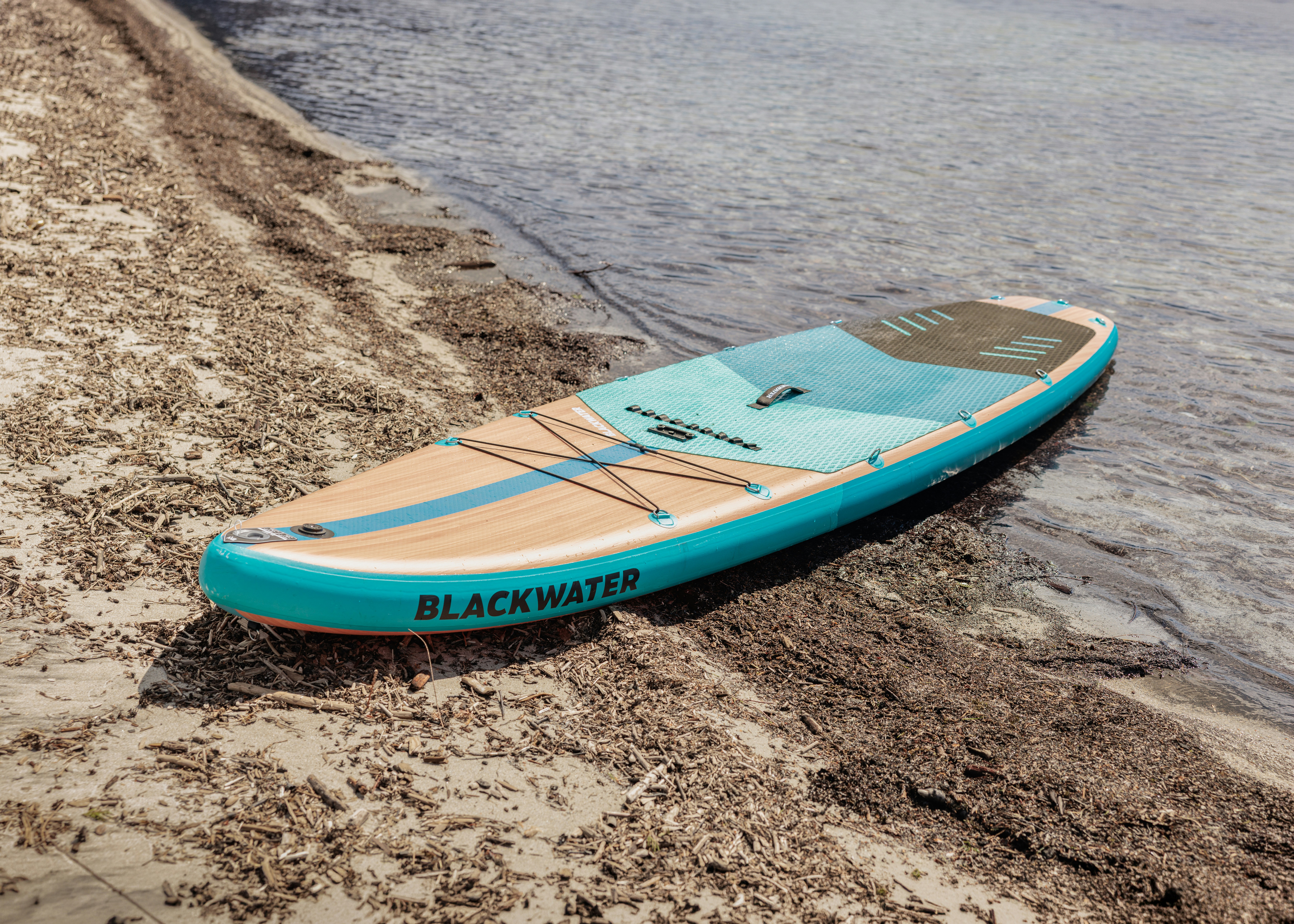 A stand-up paddleboard rests on a sandy shore.