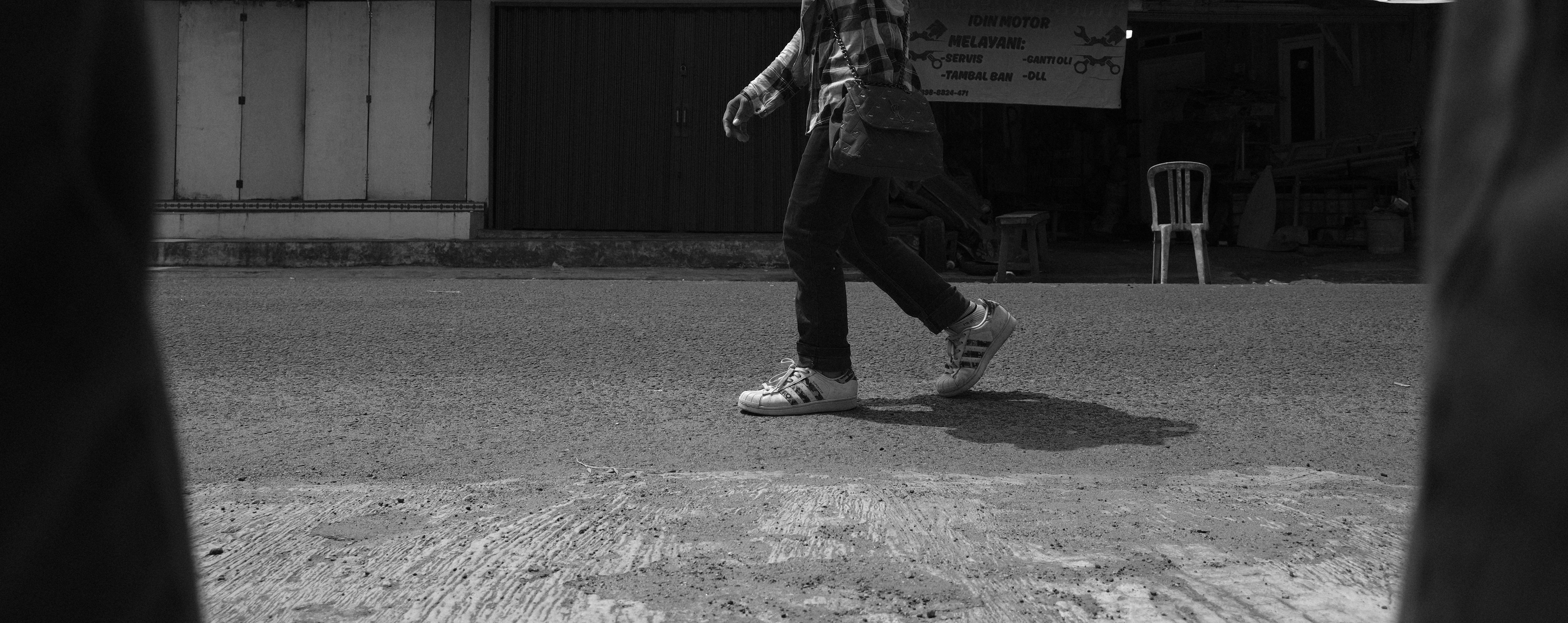 Person walking on a dusty street in black and white.