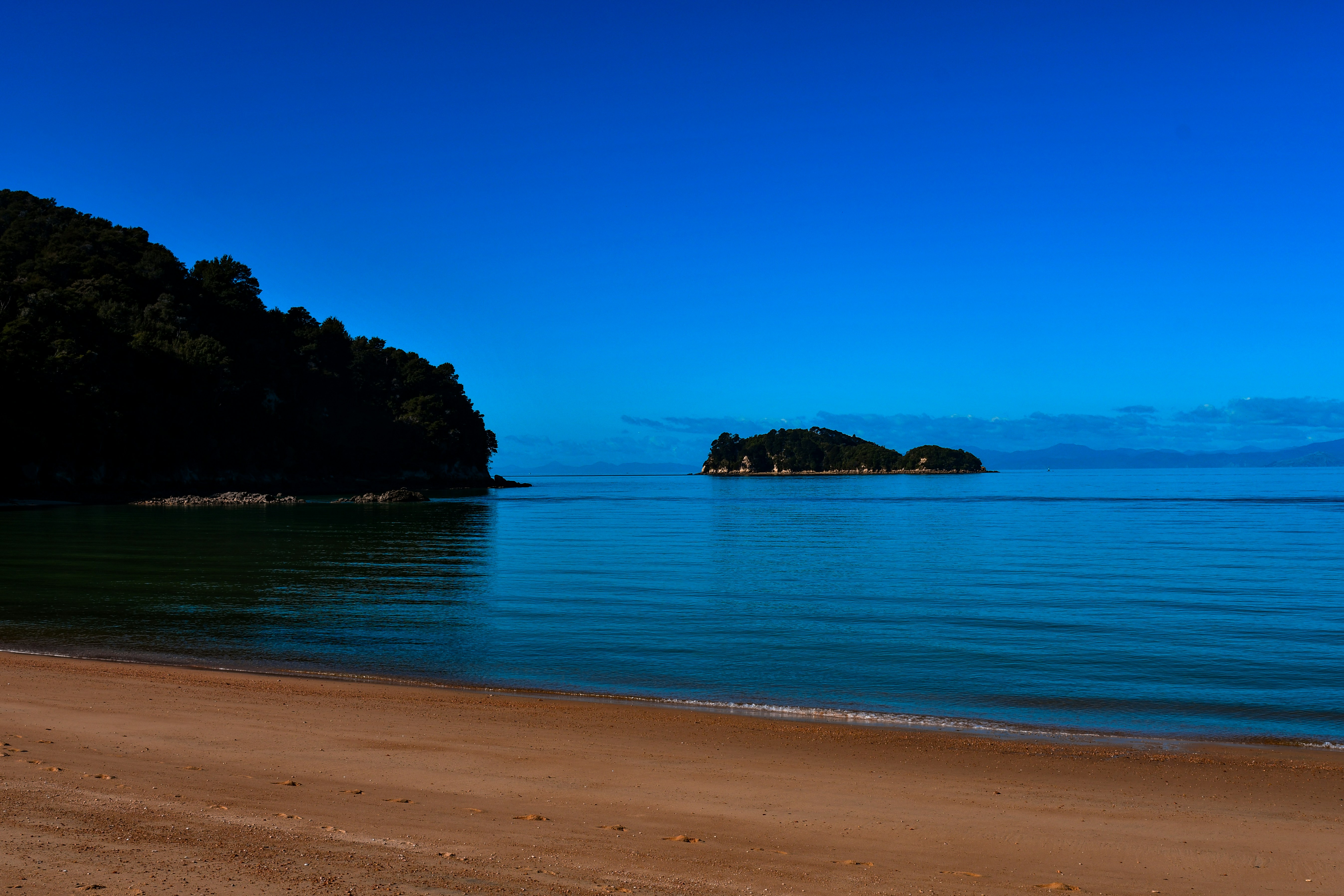 Sandy beach with calm blue ocean and distant island.