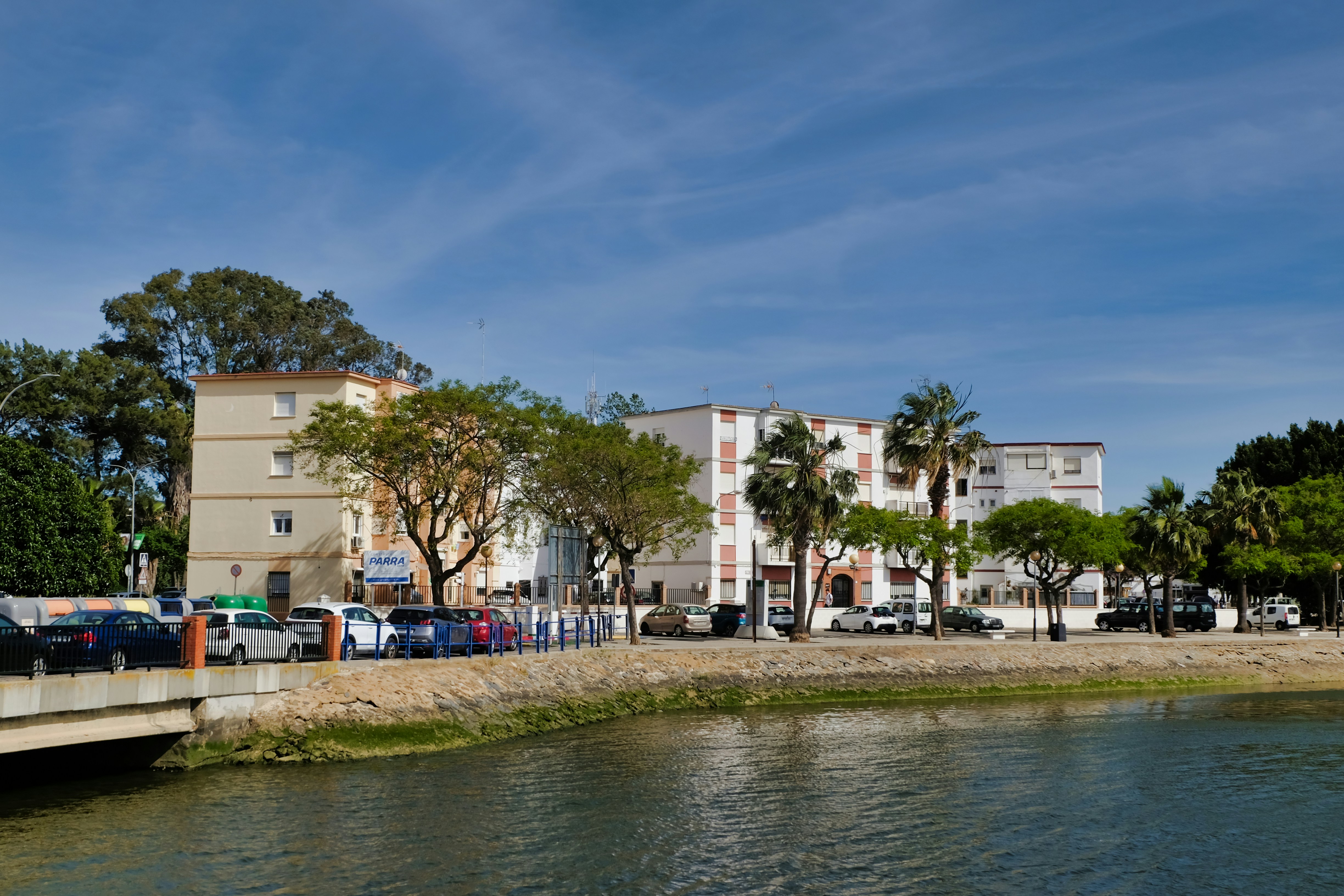Des bâtiments et des arbres bordent un front de mer avec des voitures garées.