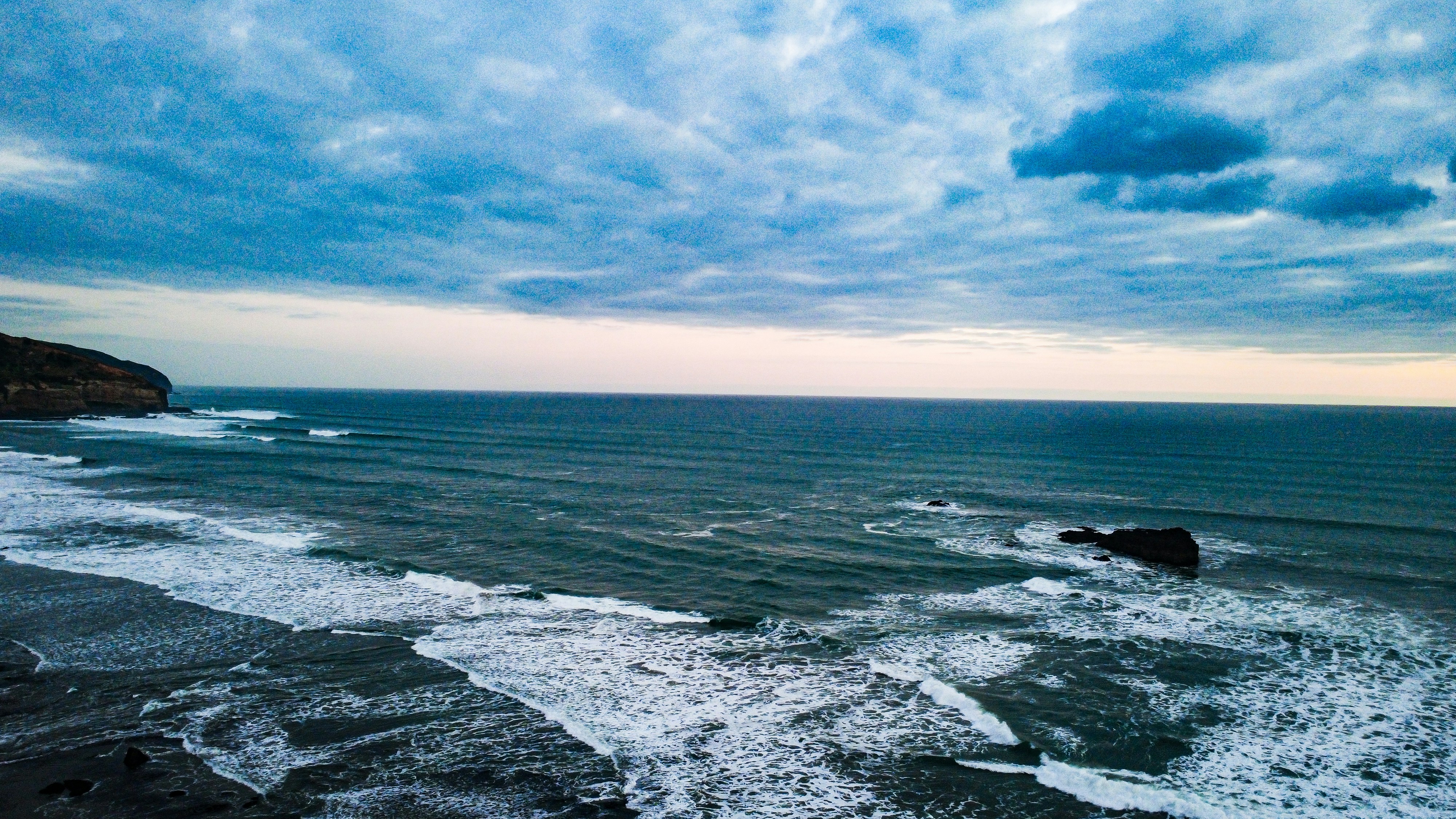Ombak menghantam pantai berbatu di bawah langit mendung