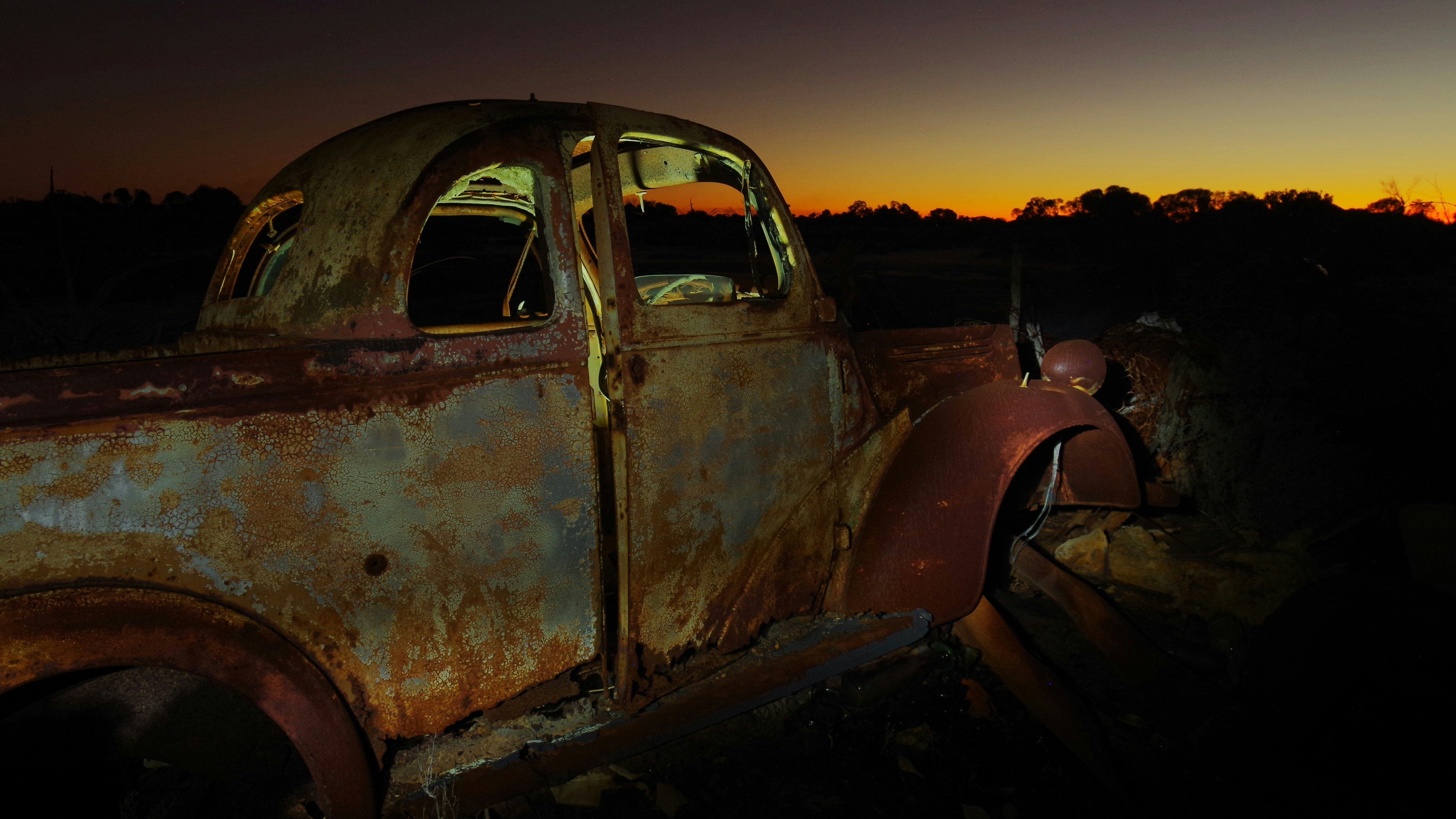 Carro abandonado enferrujado ao pôr do sol em um campo
