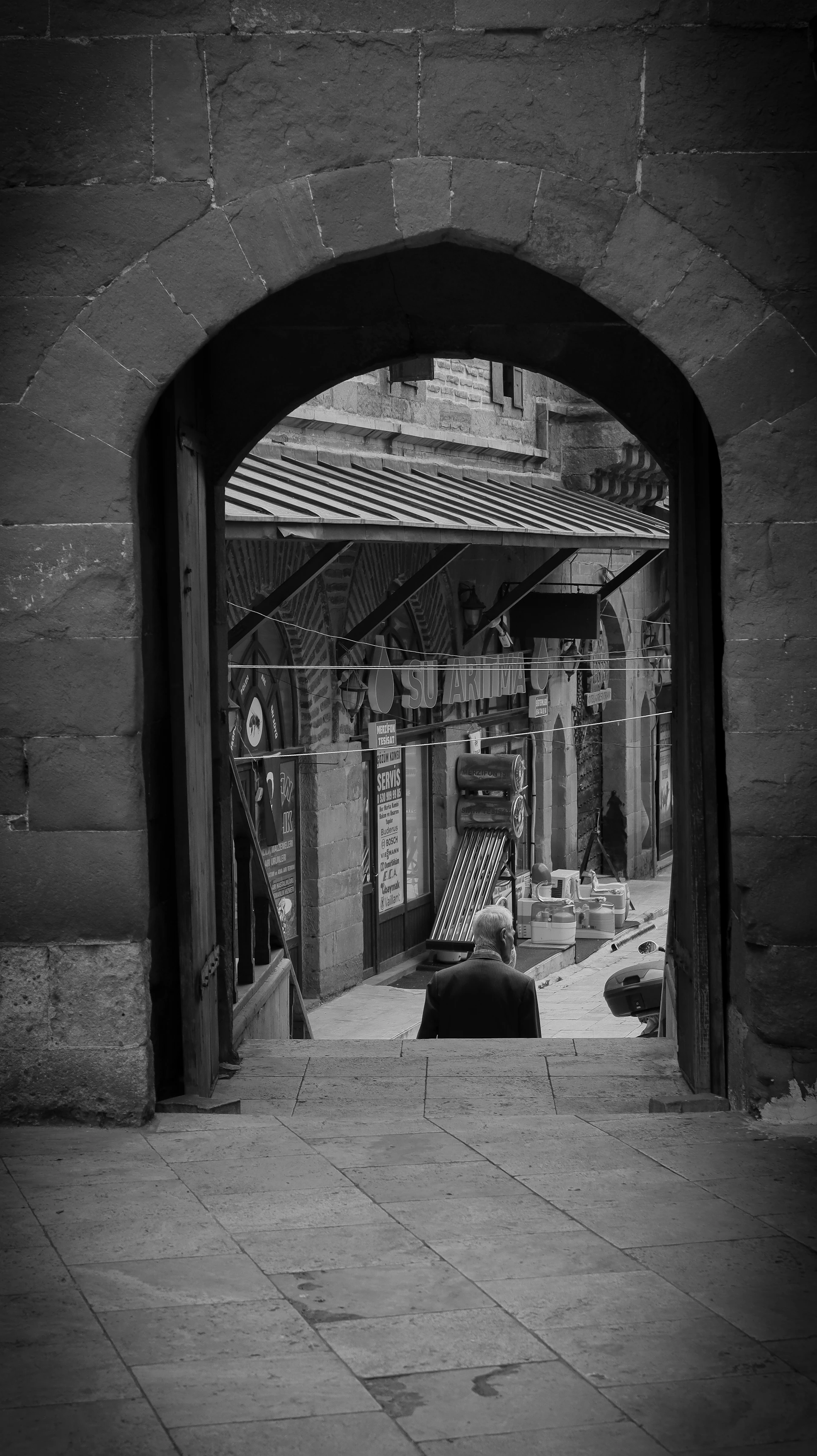 Person stands in stone archway looking down a street.
