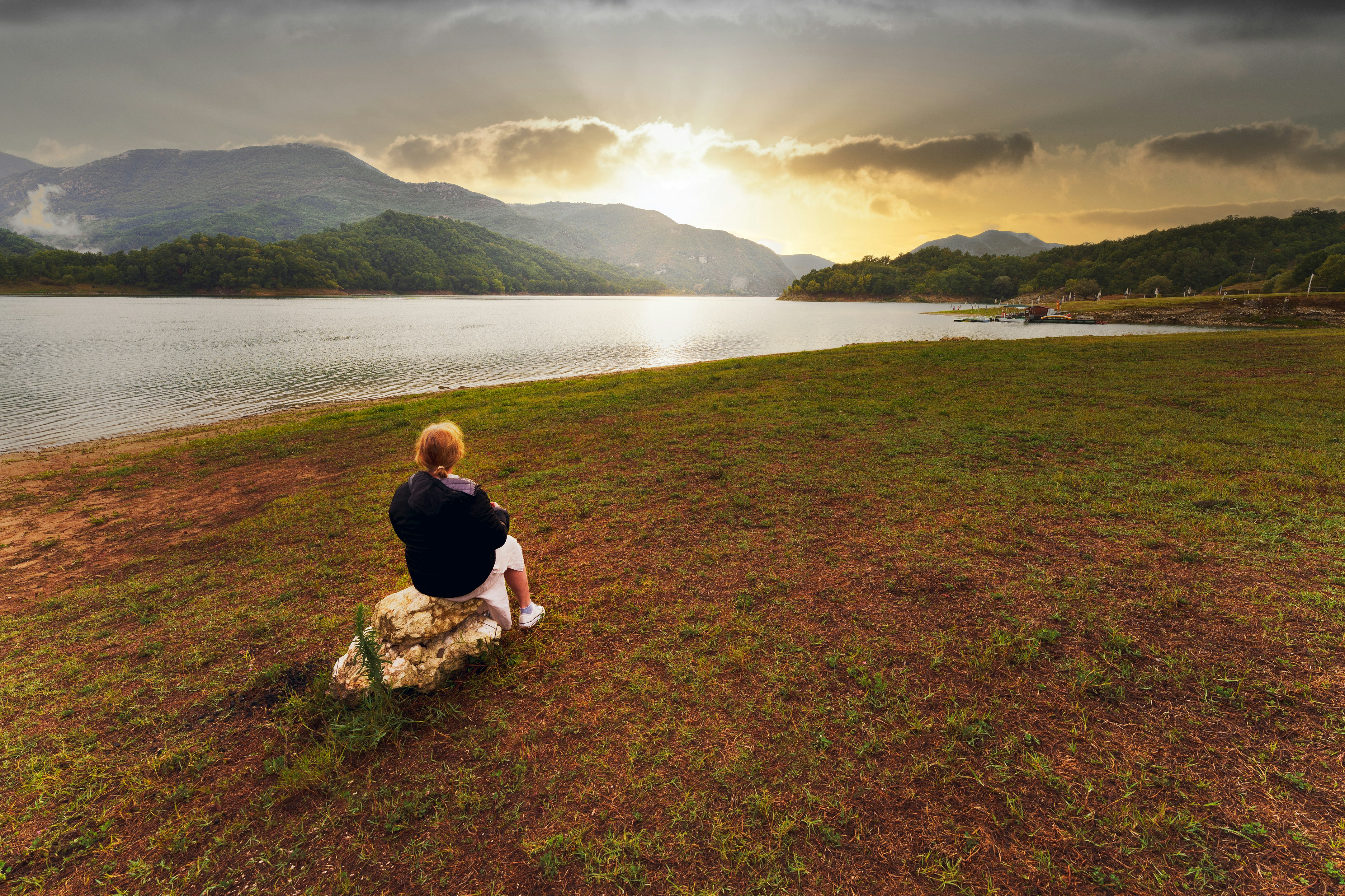 Woman sitting on rock by lake at sunset