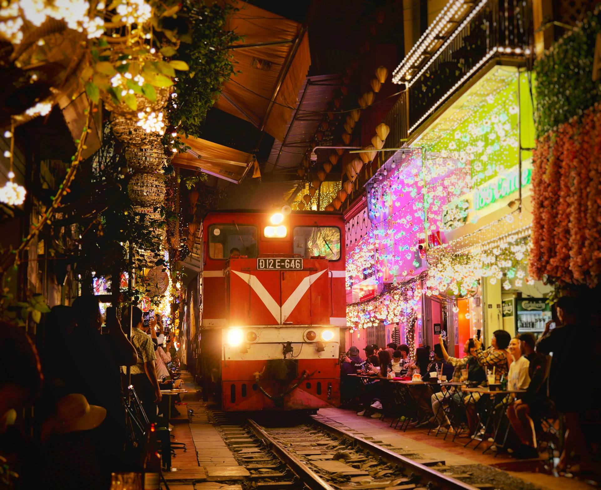 A train approaches a street lined with illuminated shops