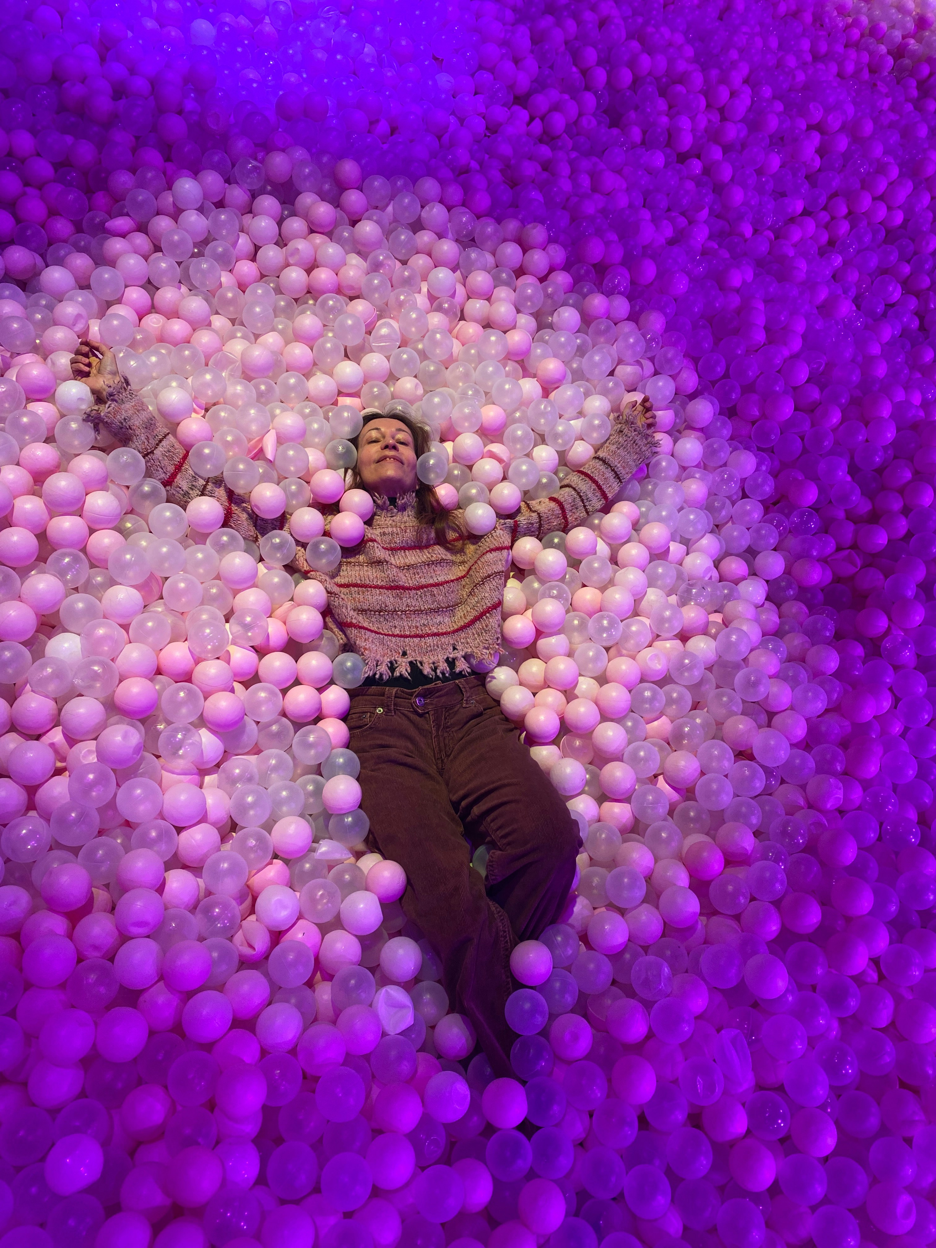 A person lies in a ball pit with purple lighting.