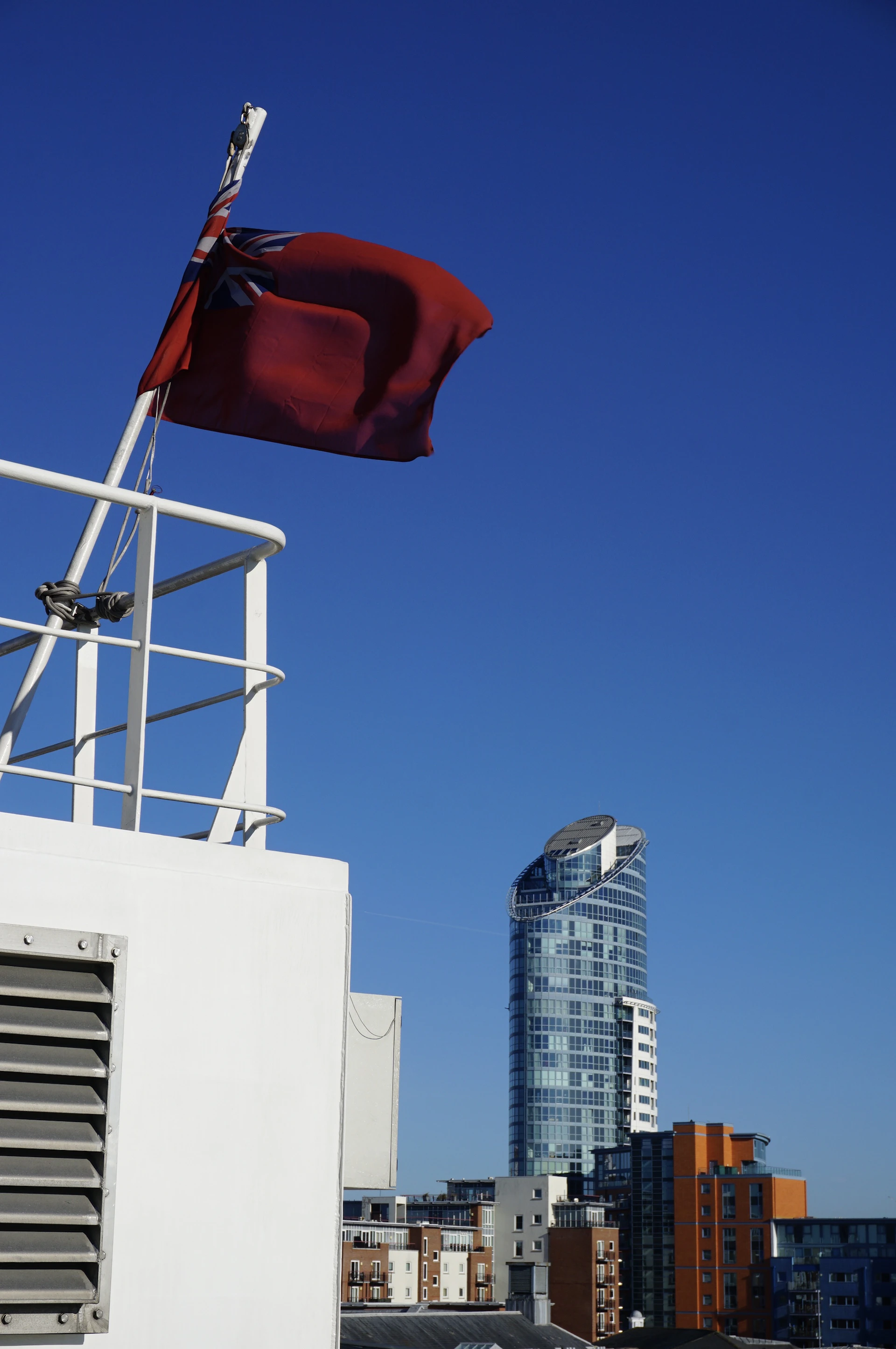 Red flag flying on a ship with city buildings behind