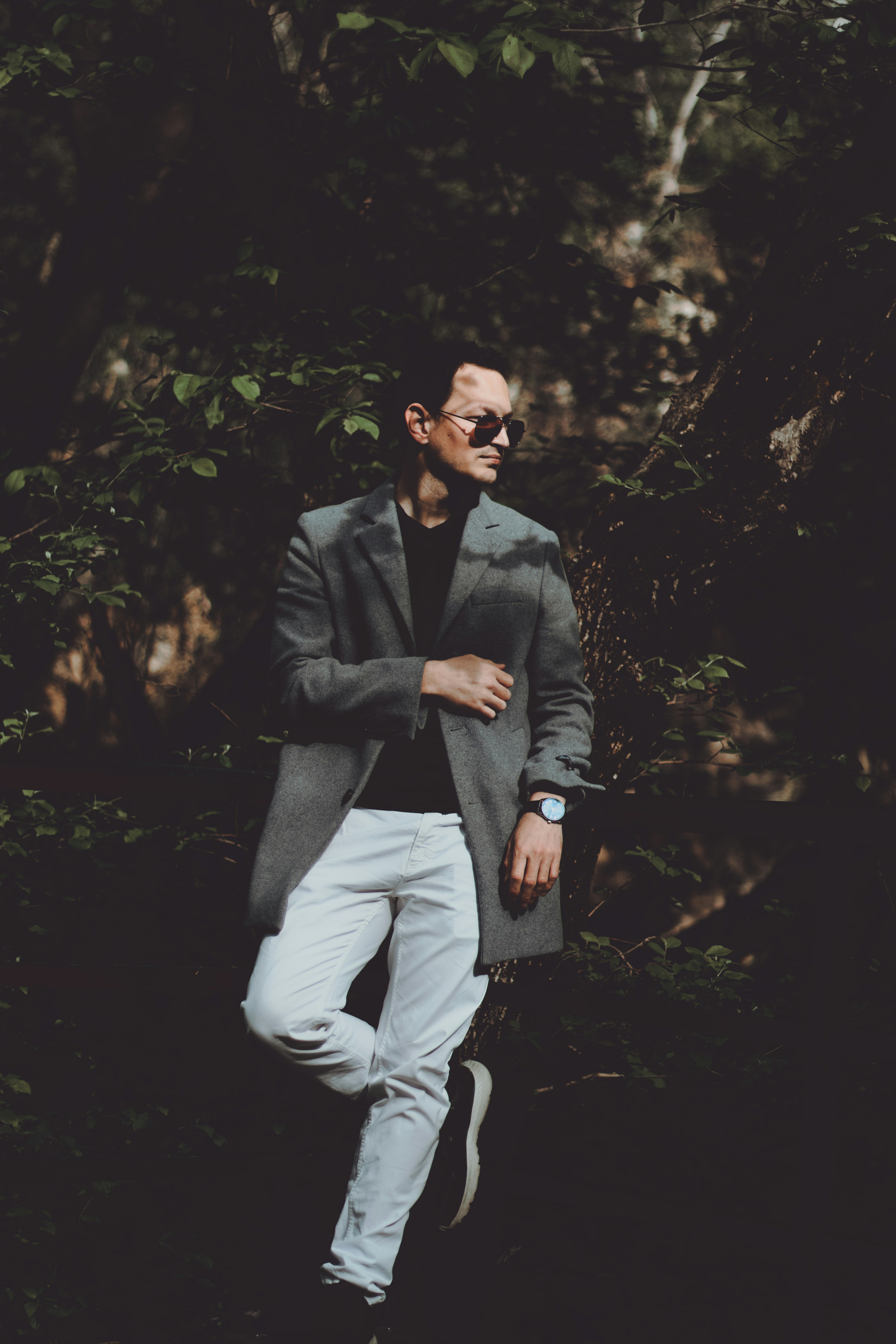 Man in coat and white pants standing near trees