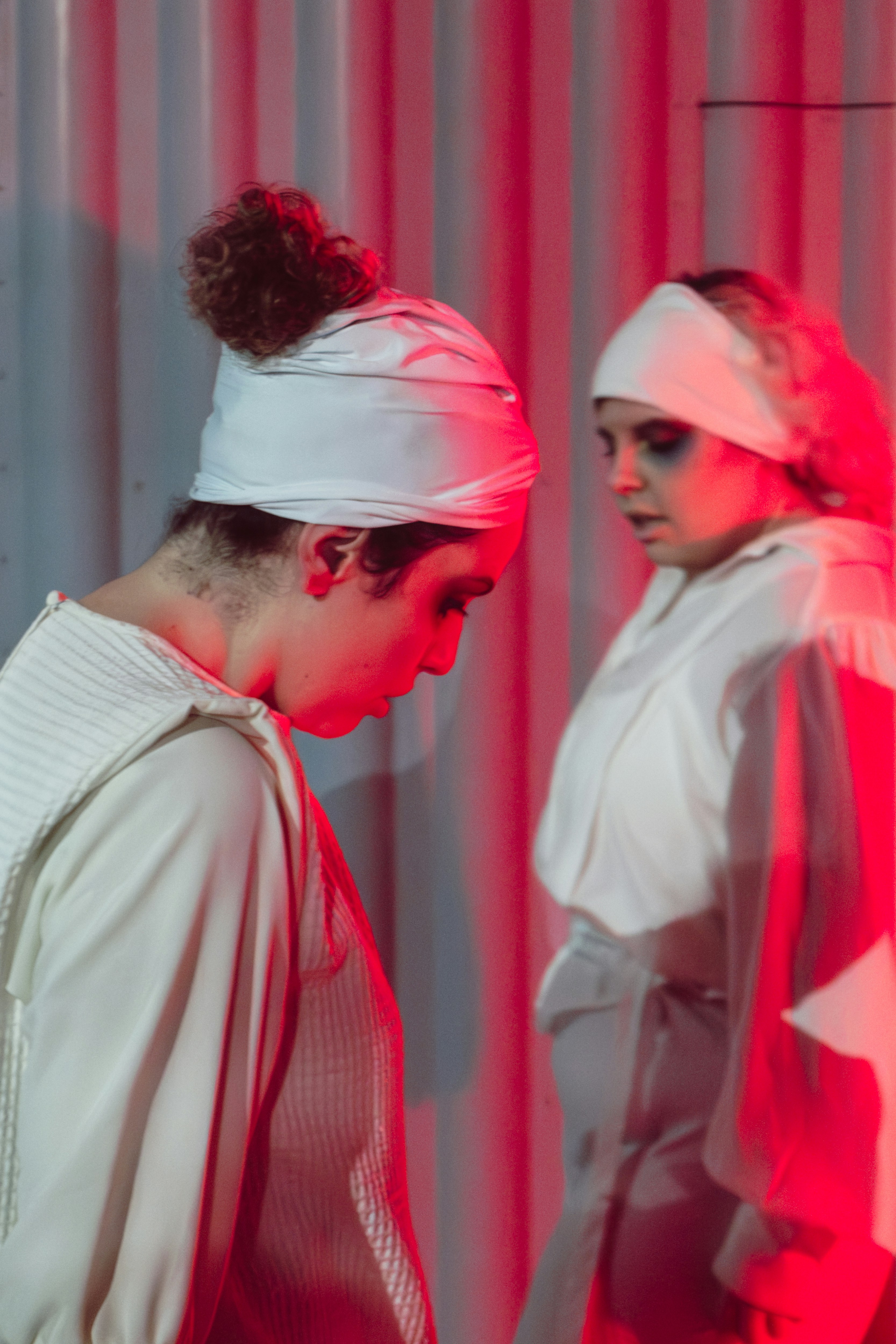 Deux artistes en costumes blancs sous un éclairage rouge dramatique.